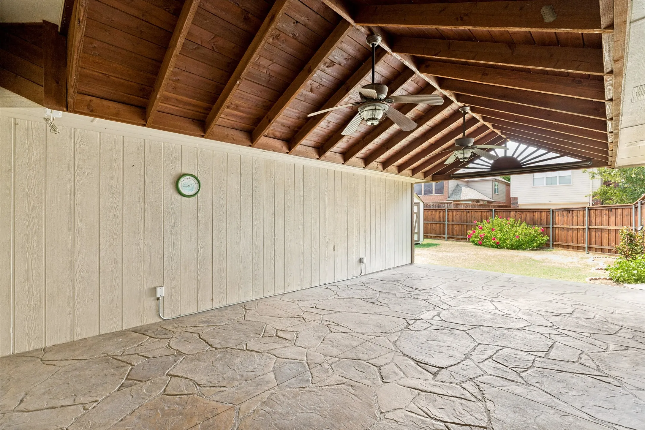 Covered patio with exposed wood beam ceiling and ceiling fan, anchored by a spacious stamped concrete floor