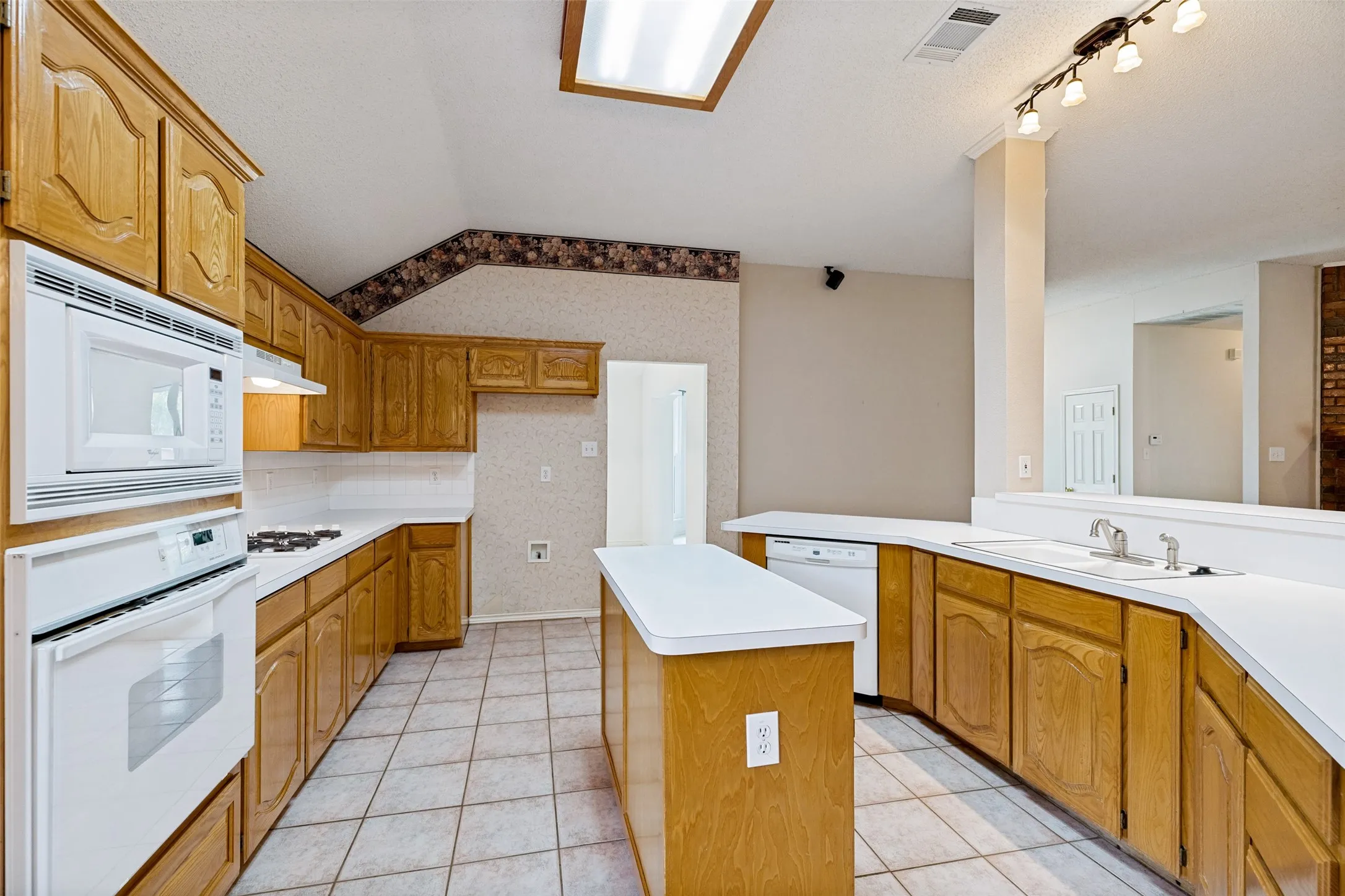 Spacious kitchen featuring wood cabinetry, white appliances, ceramic tile flooring, a centered island with counter seating, and abundant counter space