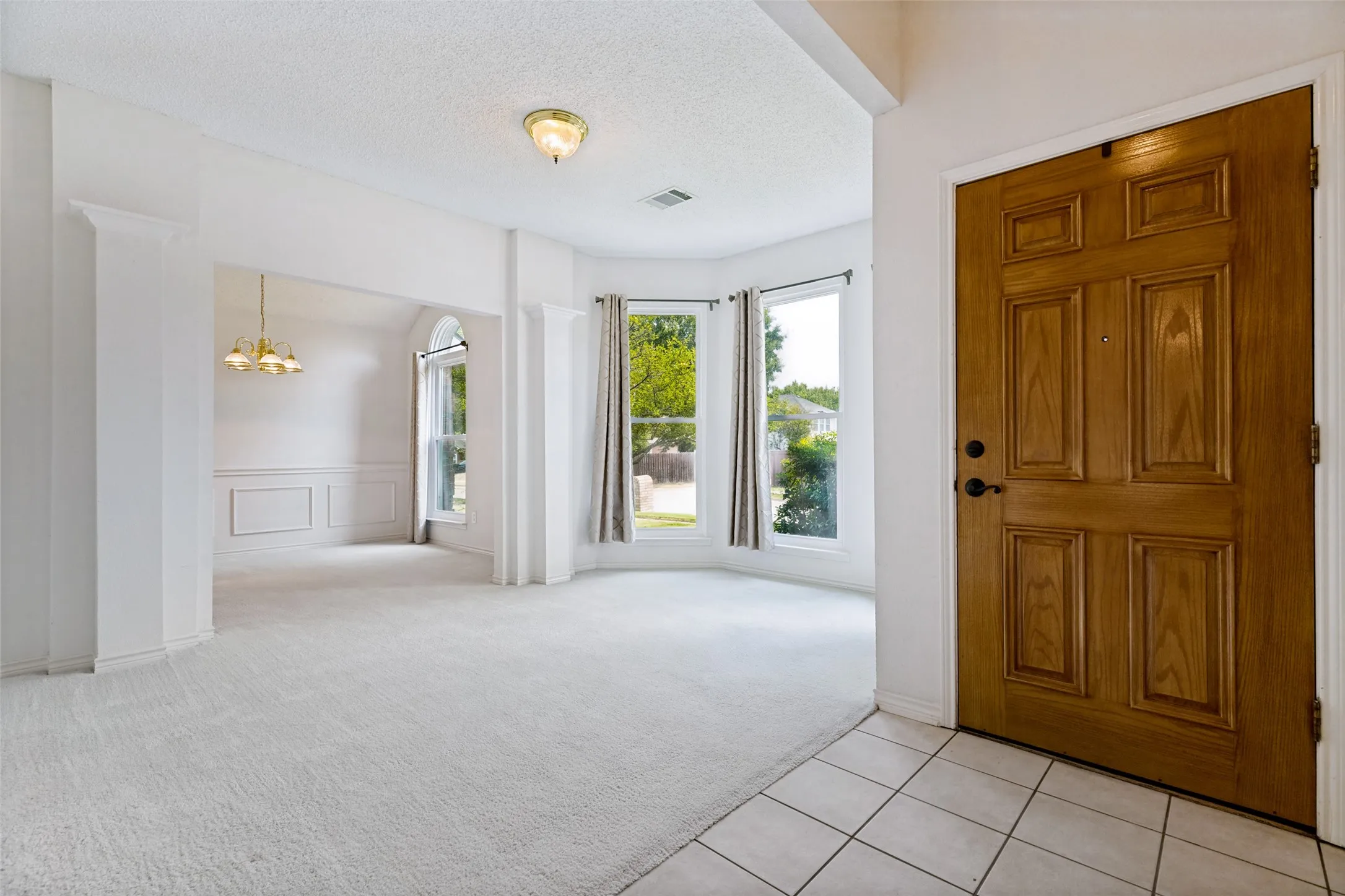 Bright, open foyer showcasing gleaming tile flooring, abundant natural light from multi-pane glass doors and windows, soaring ceilings with recessed lighting, and a substantial wooden entry door with detailed panel work