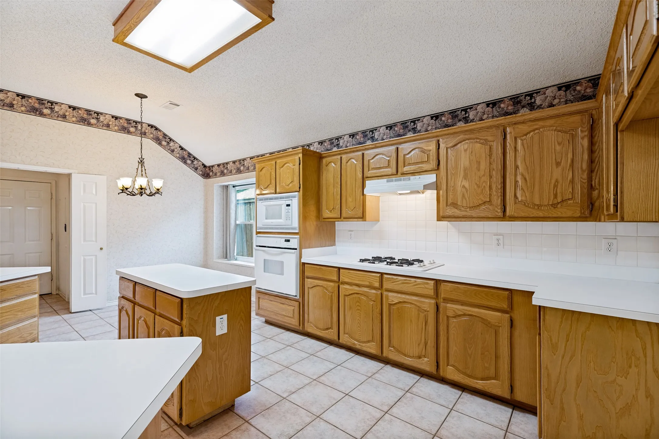 Spacious kitchen featuring wood-finish cabinetry, white countertops, tile flooring, and a central island with prep space