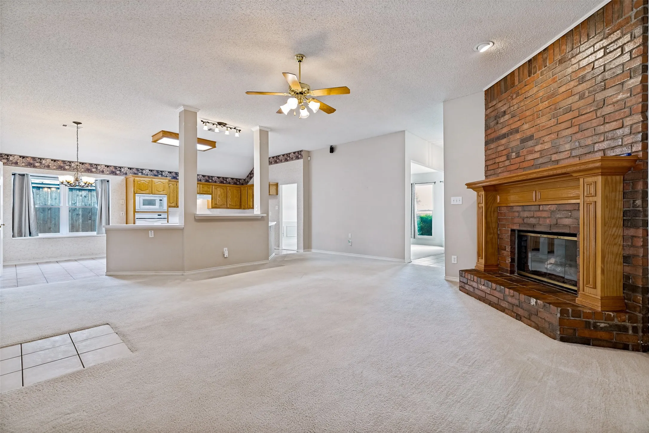 Brick fireplace with a wood mantel, light-toned carpeting, and a ceiling fan