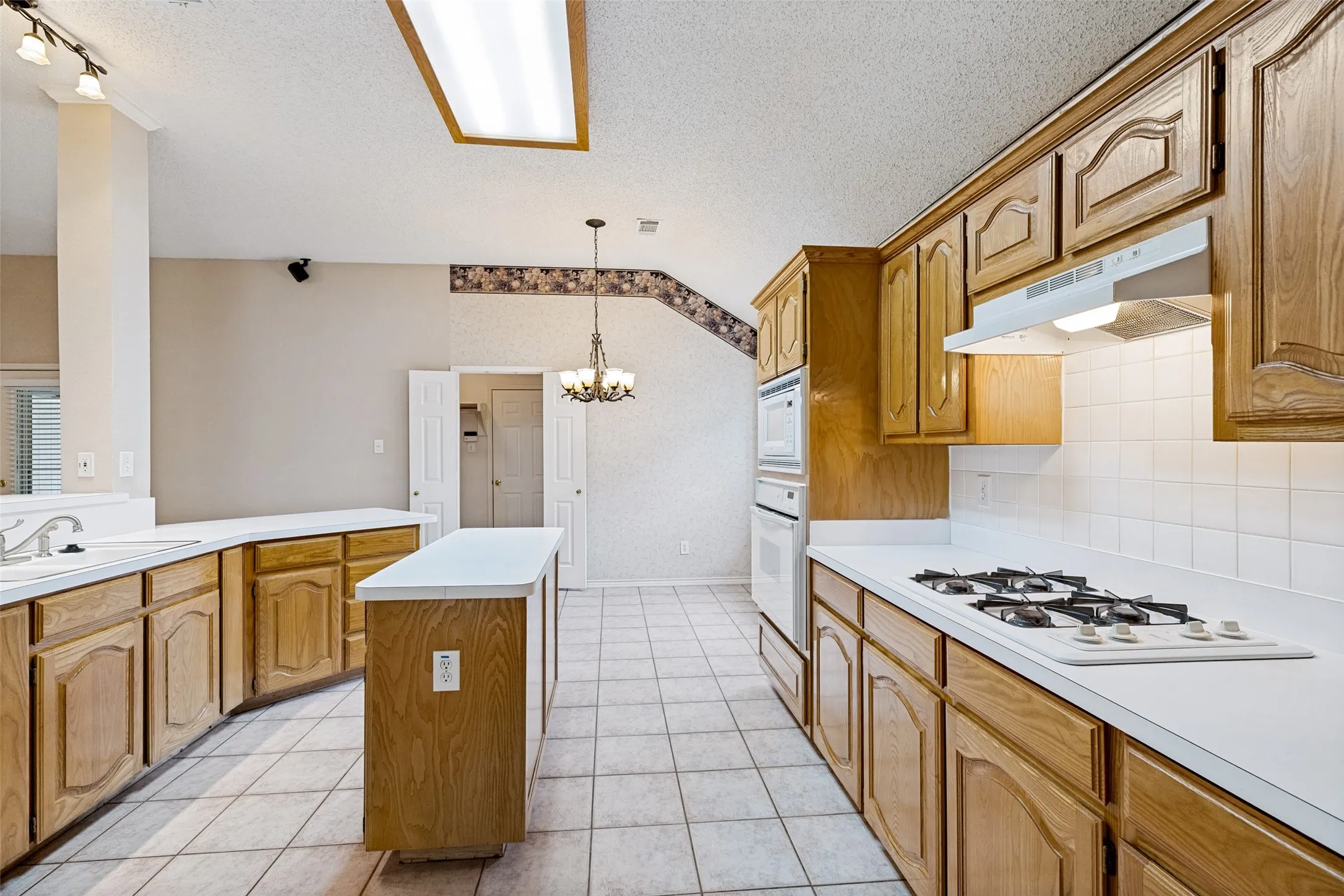 Spacious kitchen featuring wood-finish cabinetry, white tile flooring, a central island with counter seating, gas cooktop, built-in wall oven, and abundant counter space