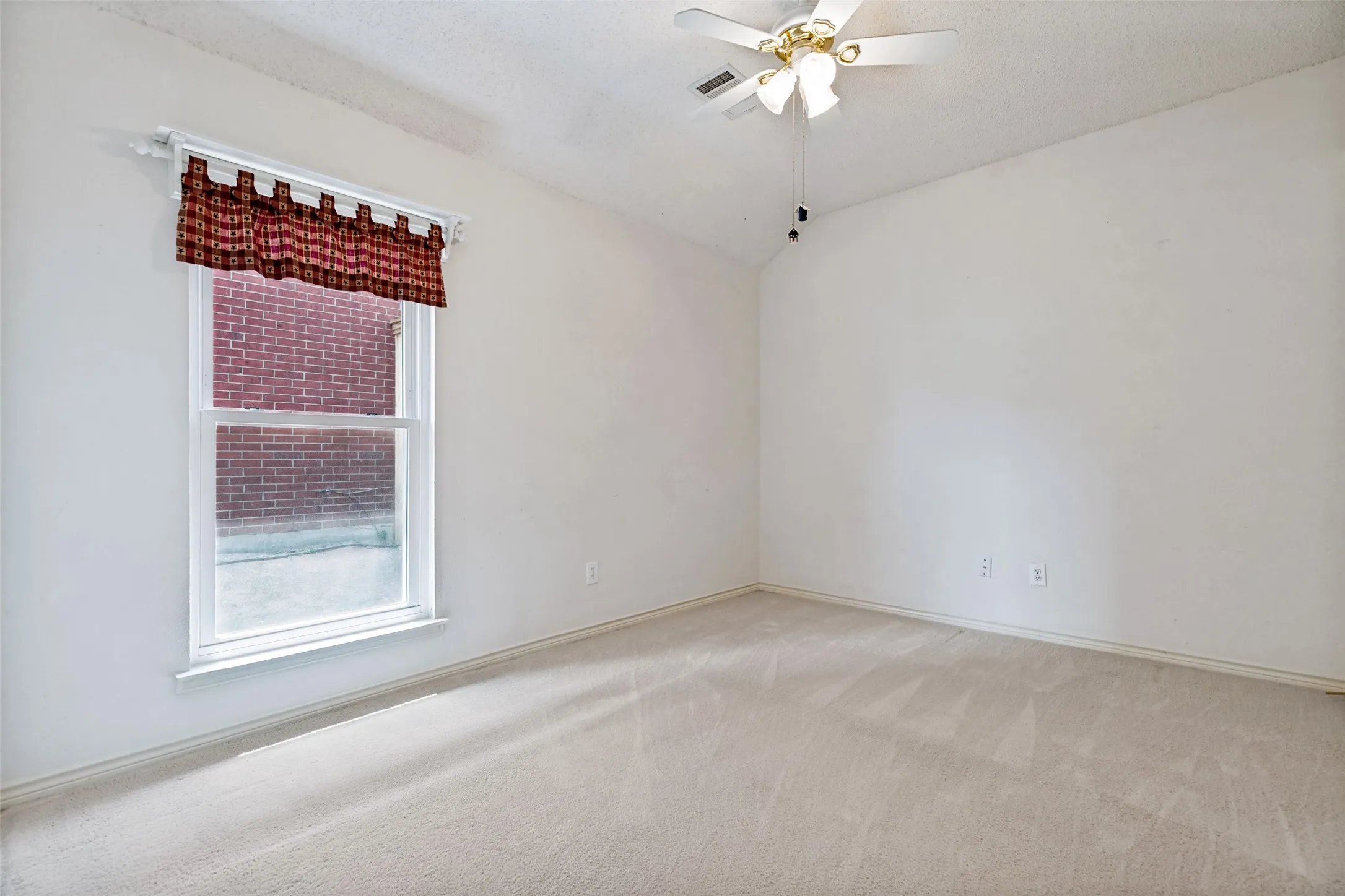 Carpeted flooring, vaulted ceiling, white walls, and a ceiling fan with light fixture