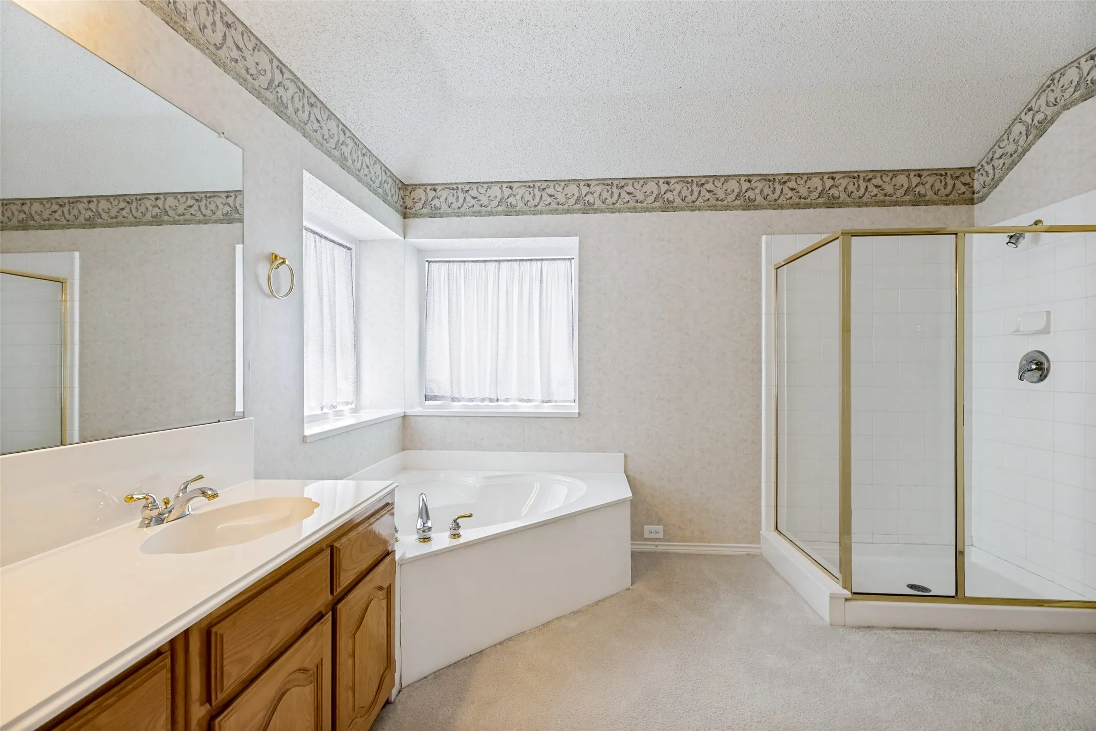 Spa-inspired primary bathroom featuring a freestanding soaking tub positioned at a bay window, dual-sink vanity with wood cabinetry and countertop, and a frameless glass-enclosed shower enclosure