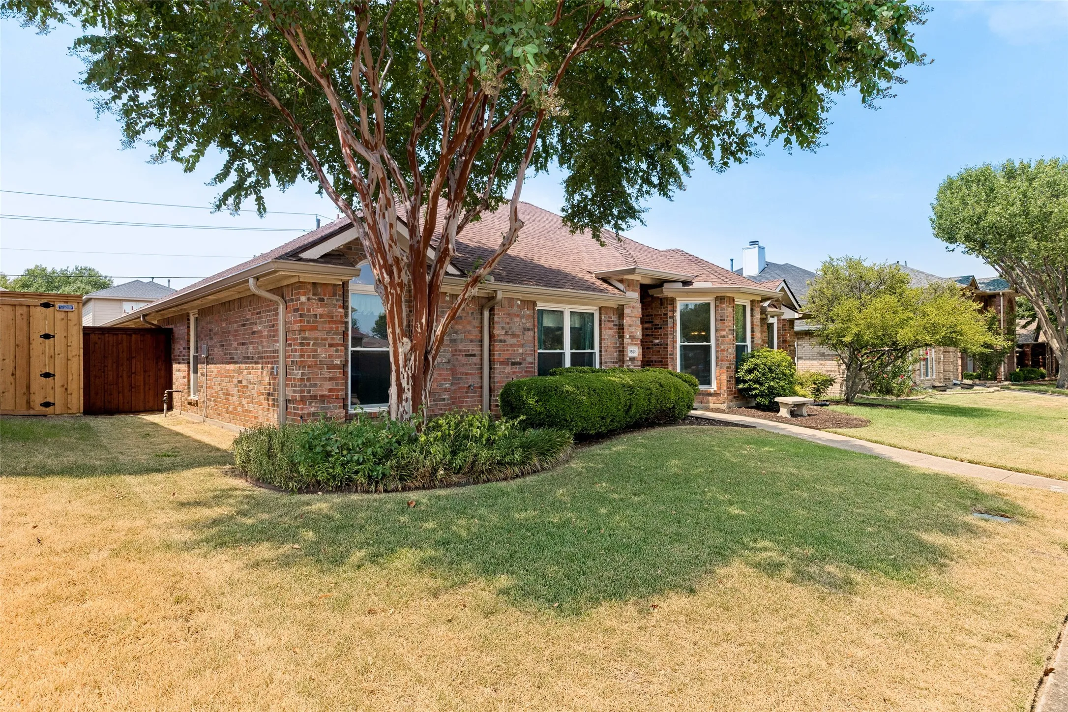 Charming brick residence featuring a mature shade tree anchoring the front landscaping, manicured lawn, and established shrub beds