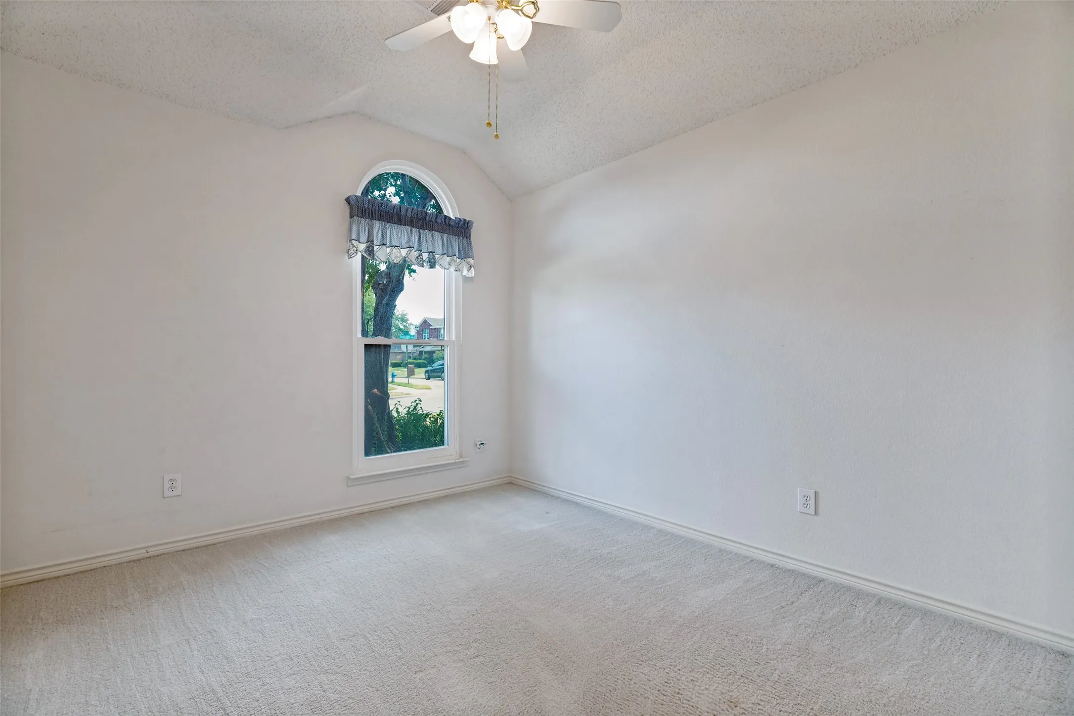 Arched window with decorative valance, sloped ceiling, and ceiling fan with integrated lighting