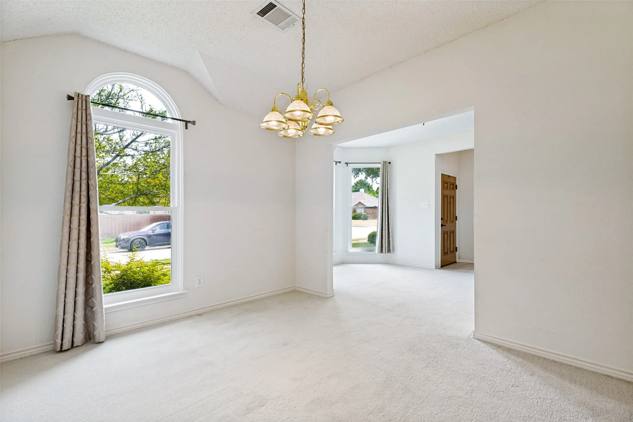 Bright, open dining oom showcasing soaring vaulted ceilings, abundant natural light from an arched transom window, and neutral carpet flooring