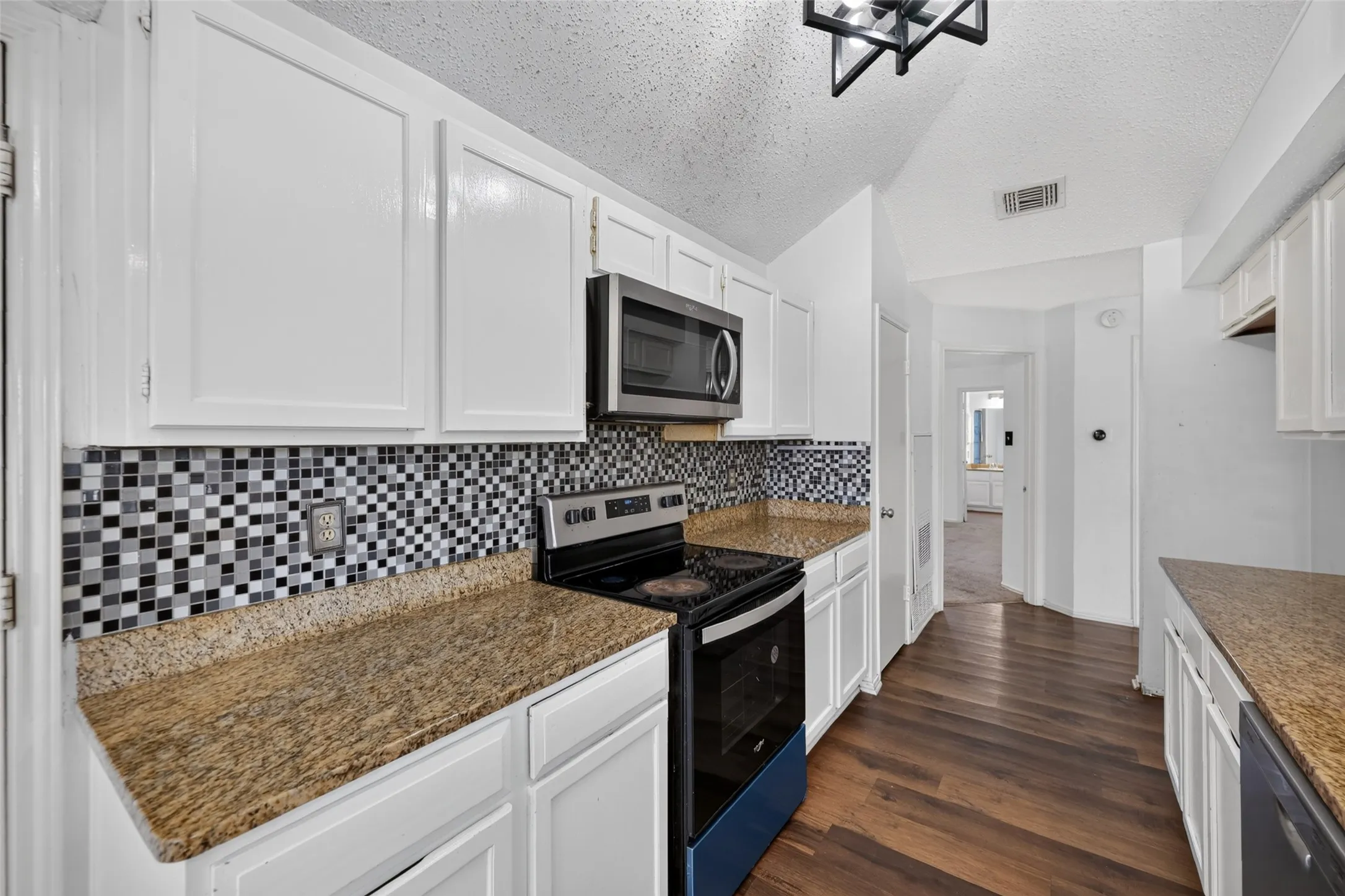 White cabinetry with matte black hardware, mosaic tile backsplash, granite-style countertops, stainless steel appliances, and wood-finish flooring