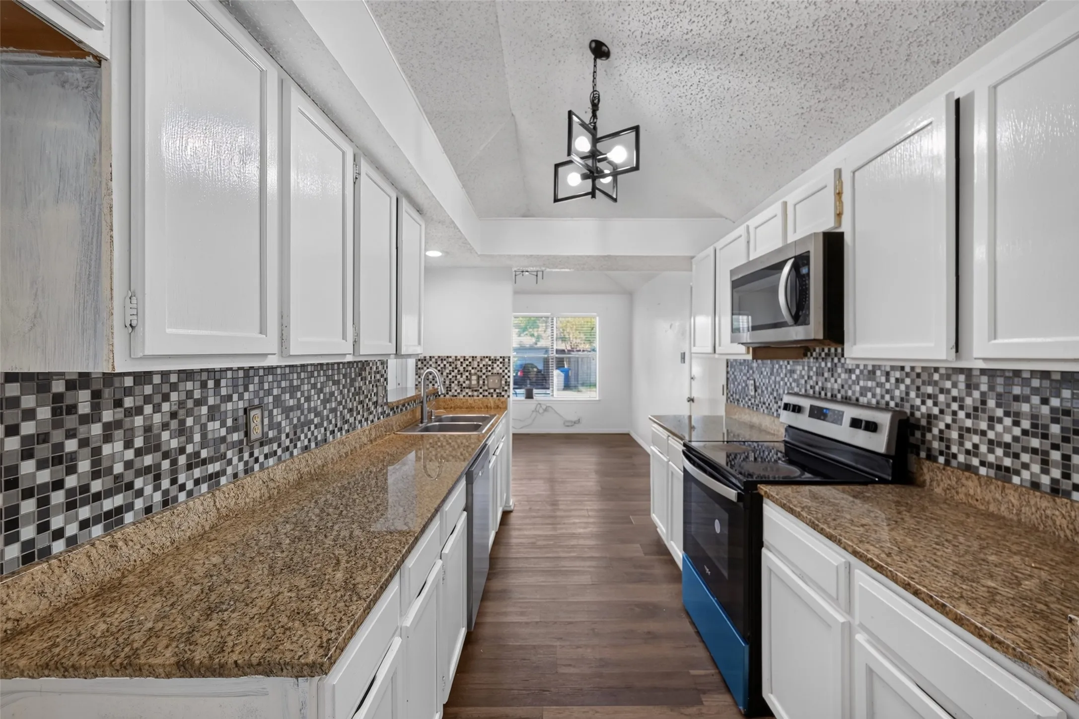 Galley kitchen featuring white cabinetry, a mosaic tile backsplash, stone-look countertops, stainless steel appliances, and wood-finish flooring