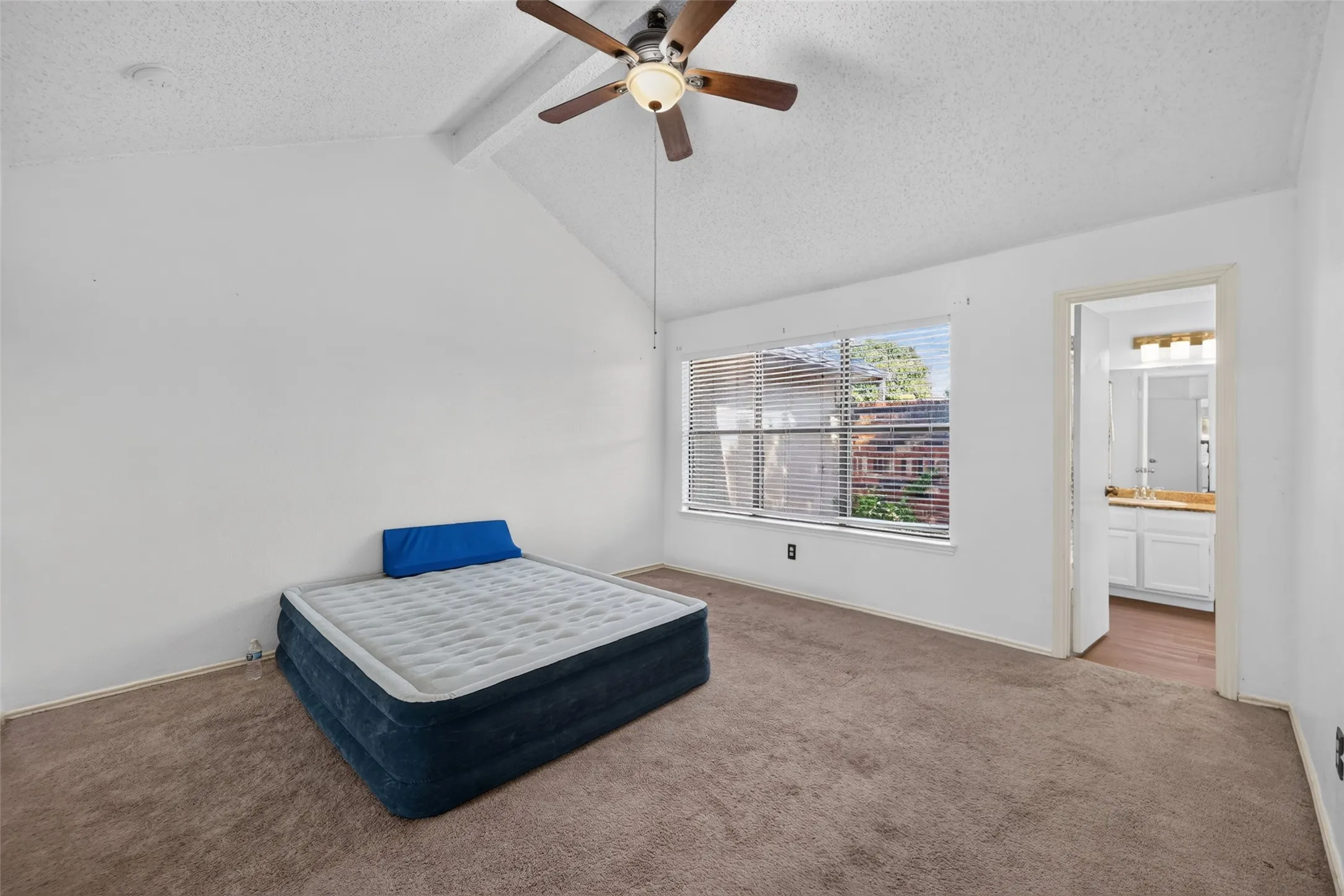 Vaulted ceiling with a ceiling fan, carpeted flooring, and a large window with horizontal blinds