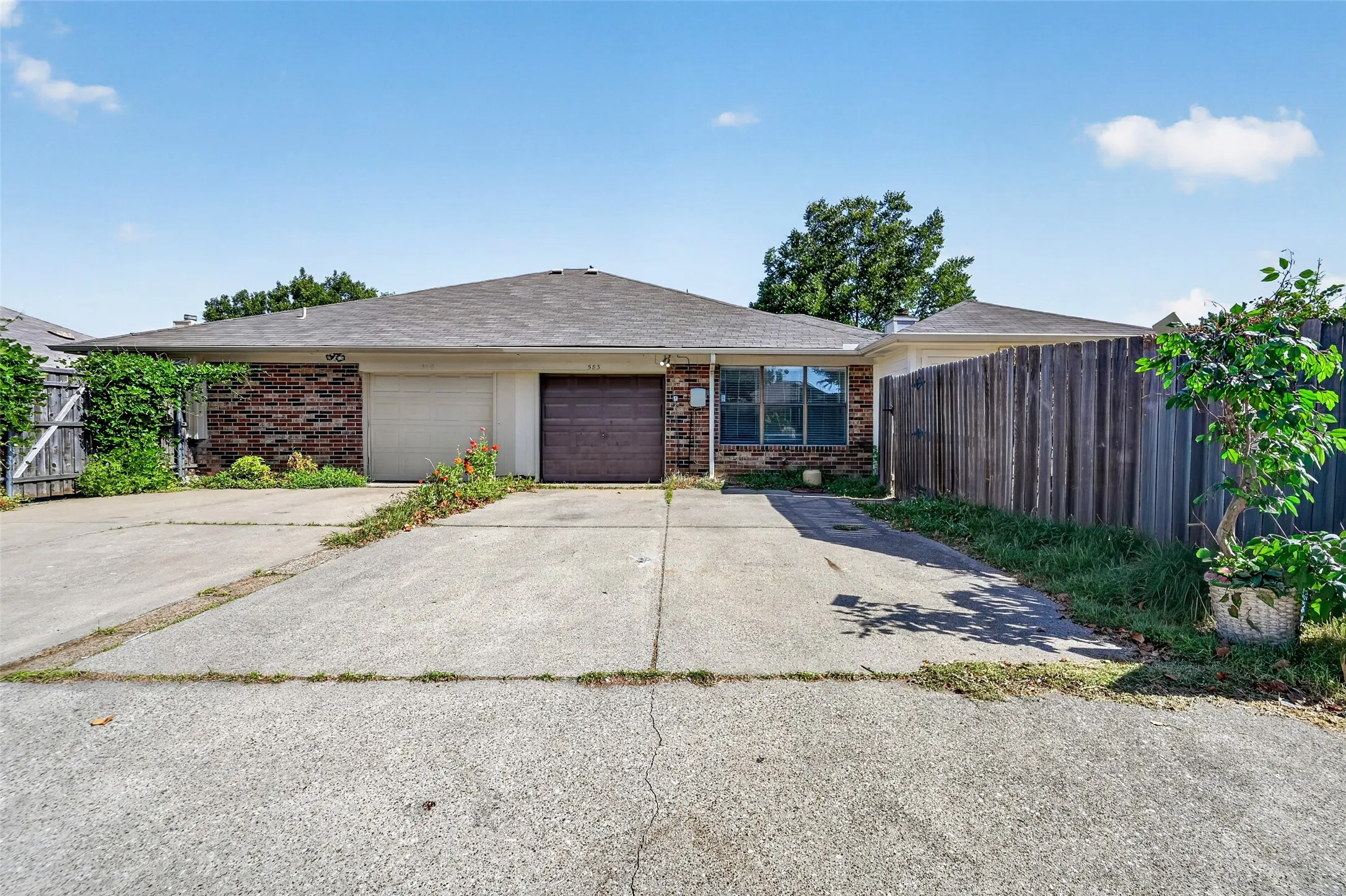 Brick facade residence with an attached garage, pitched roof, and a privacy fence