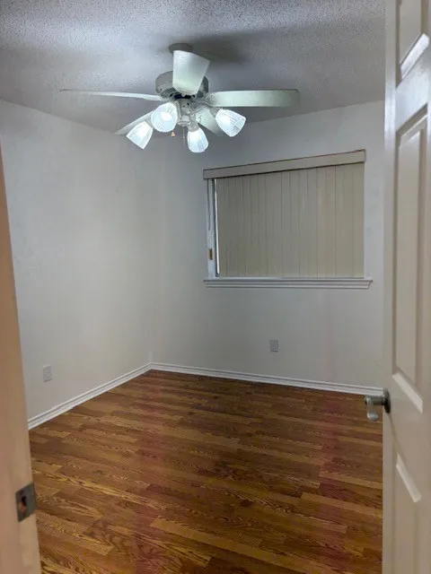 Wood-finish flooring, ceiling fan with integrated lighting, window with blinds, and white trim