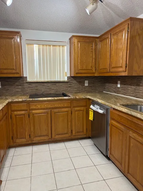 Kitchen featuring wood cabinetry, stone countertops, a tile backsplash, stainless steel appliances, and tile flooring