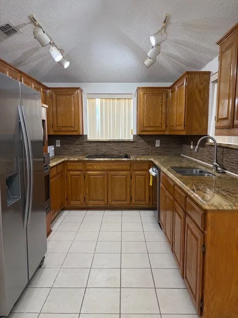 Kitchen featuring wood cabinetry, light-toned tile flooring, light-toned countertops, and a stainless steel sink with a high-arc faucet