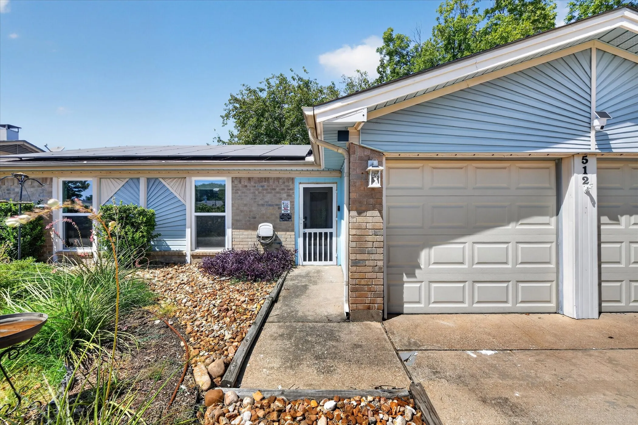 Exterior featuring light blue siding, brick accents, a paneled garage door, and a front entry with a security screen door
