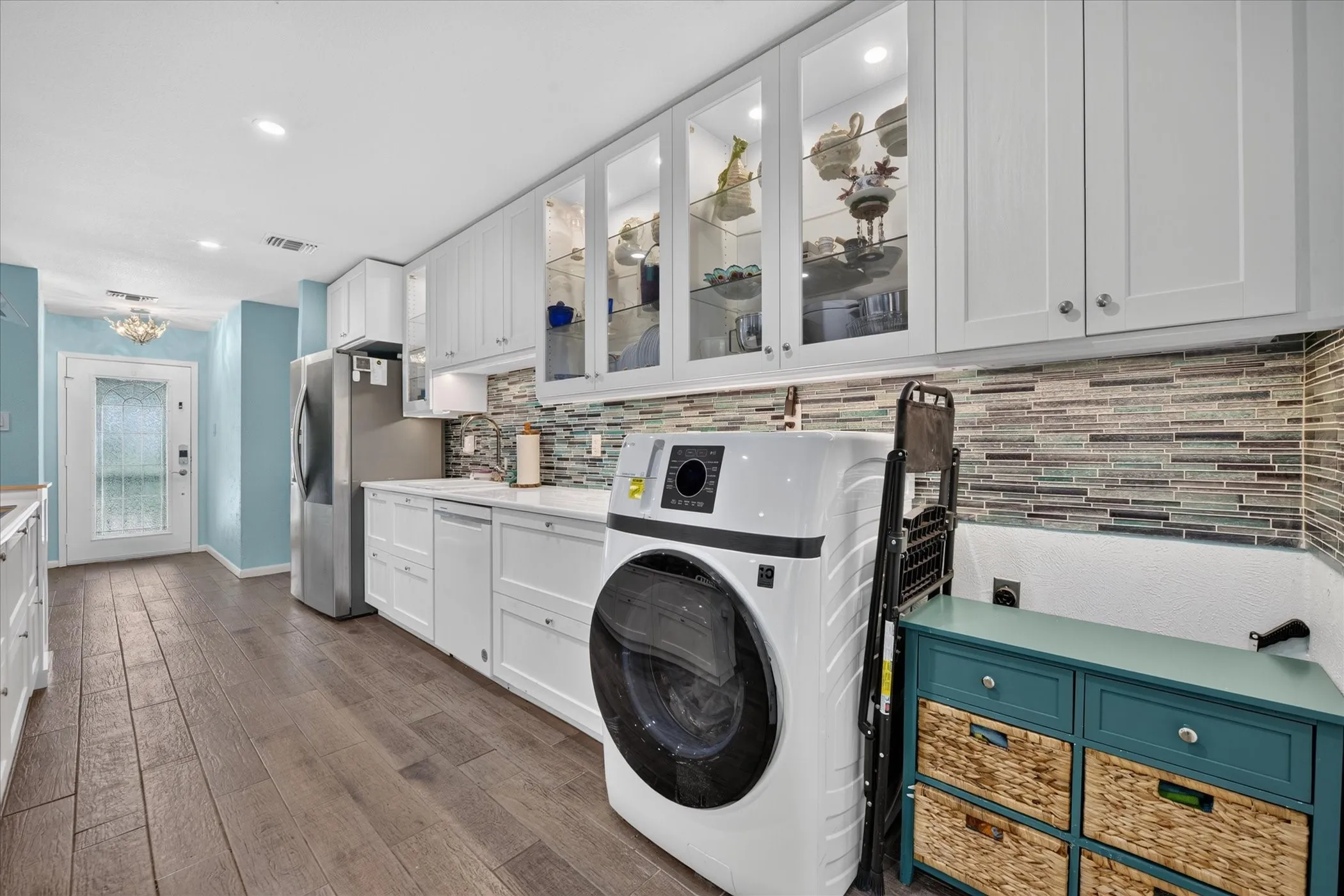 Wood-finish flooring, white cabinetry, integrated stainless steel appliances, mosaic tile backsplash, and recessed lighting