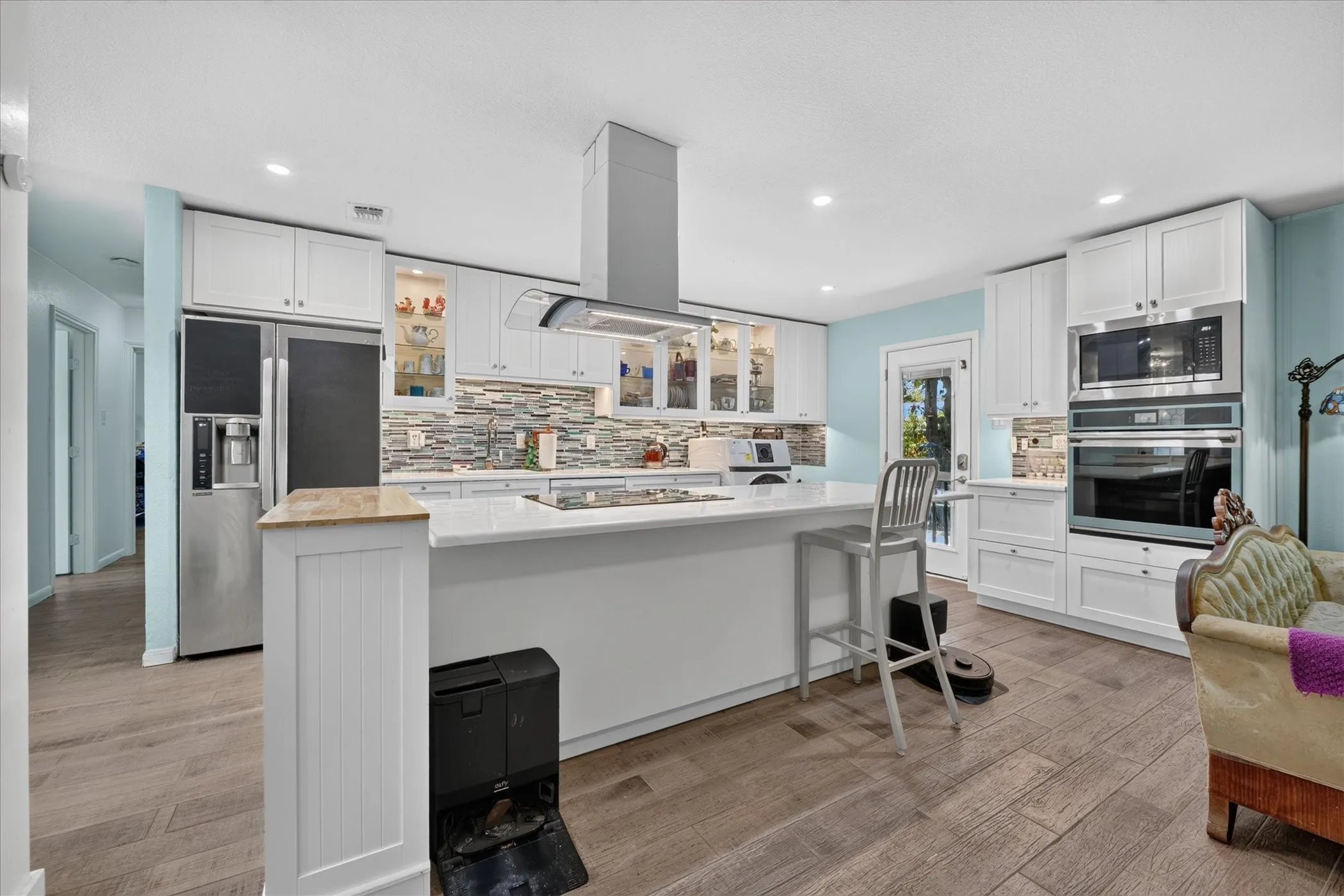 Modern kitchen featuring wood-finish flooring, white cabinetry, integrated stainless steel appliances, a center island with countertop seating, and a mosaic tile backsplash