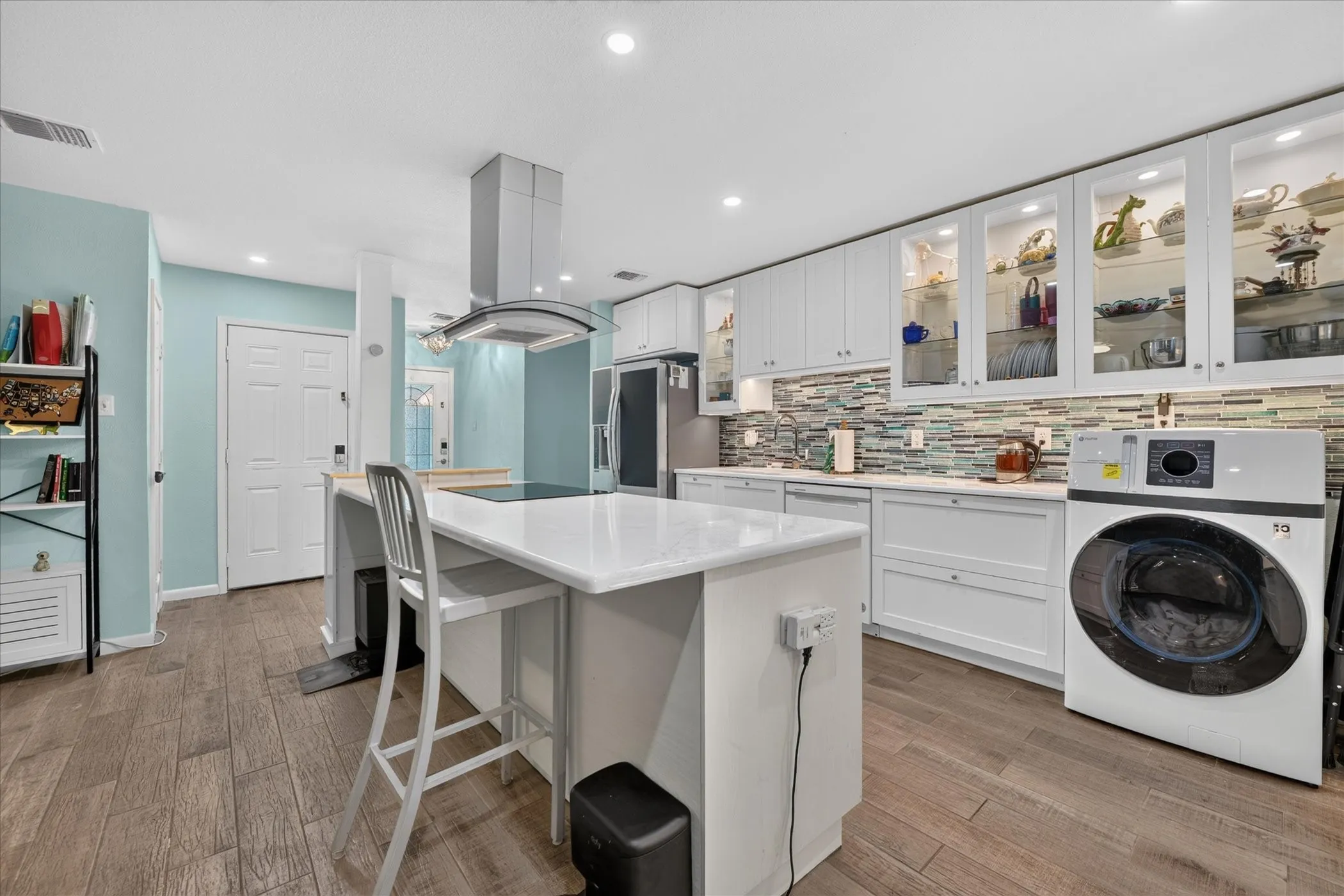 Kitchen featuring wood-finish flooring, white cabinetry, a central island with countertop seating, and a mosaic tile backsplash