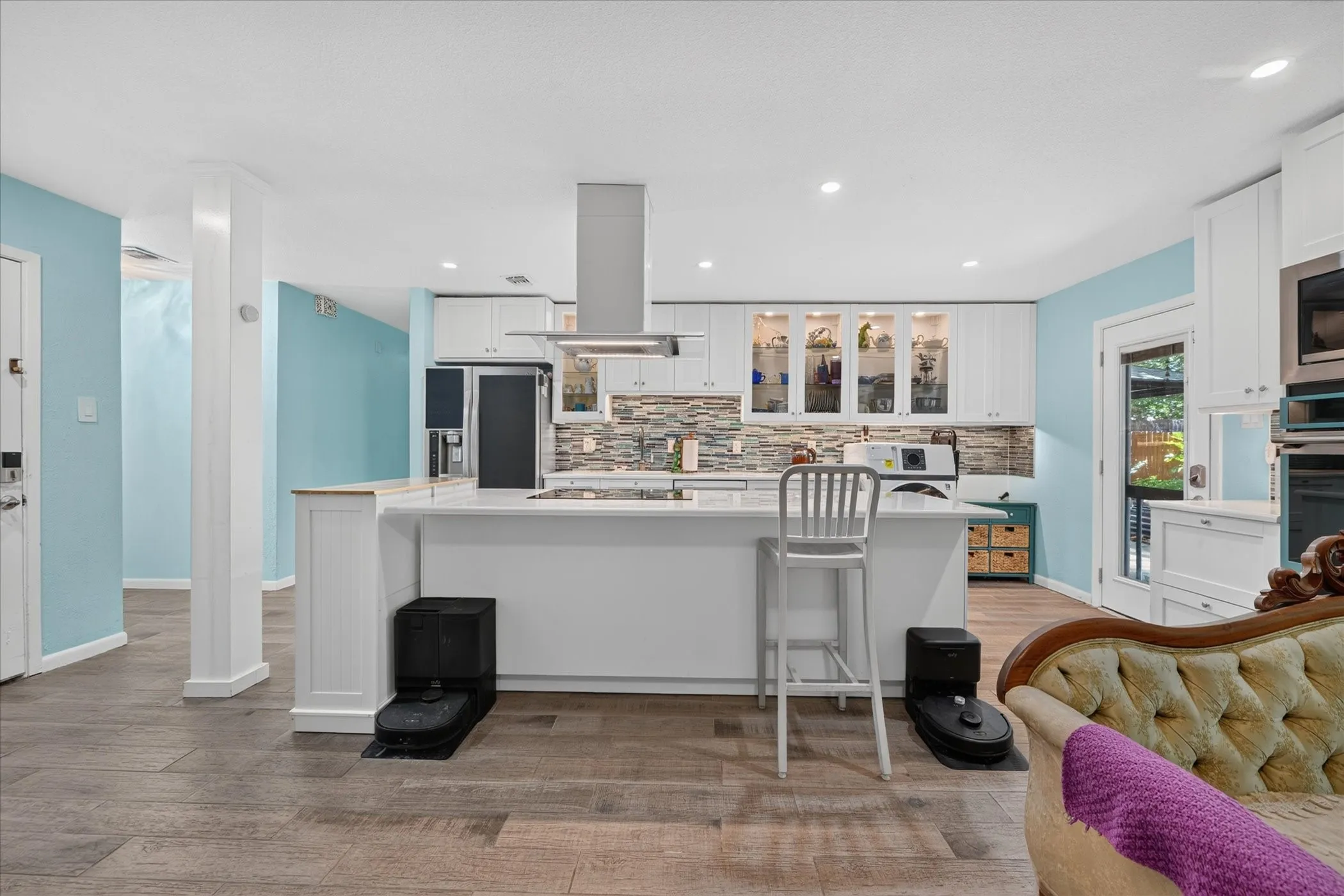 Spacious kitchen with wood-finish flooring, white cabinetry, integrated range hood, and recessed lighting