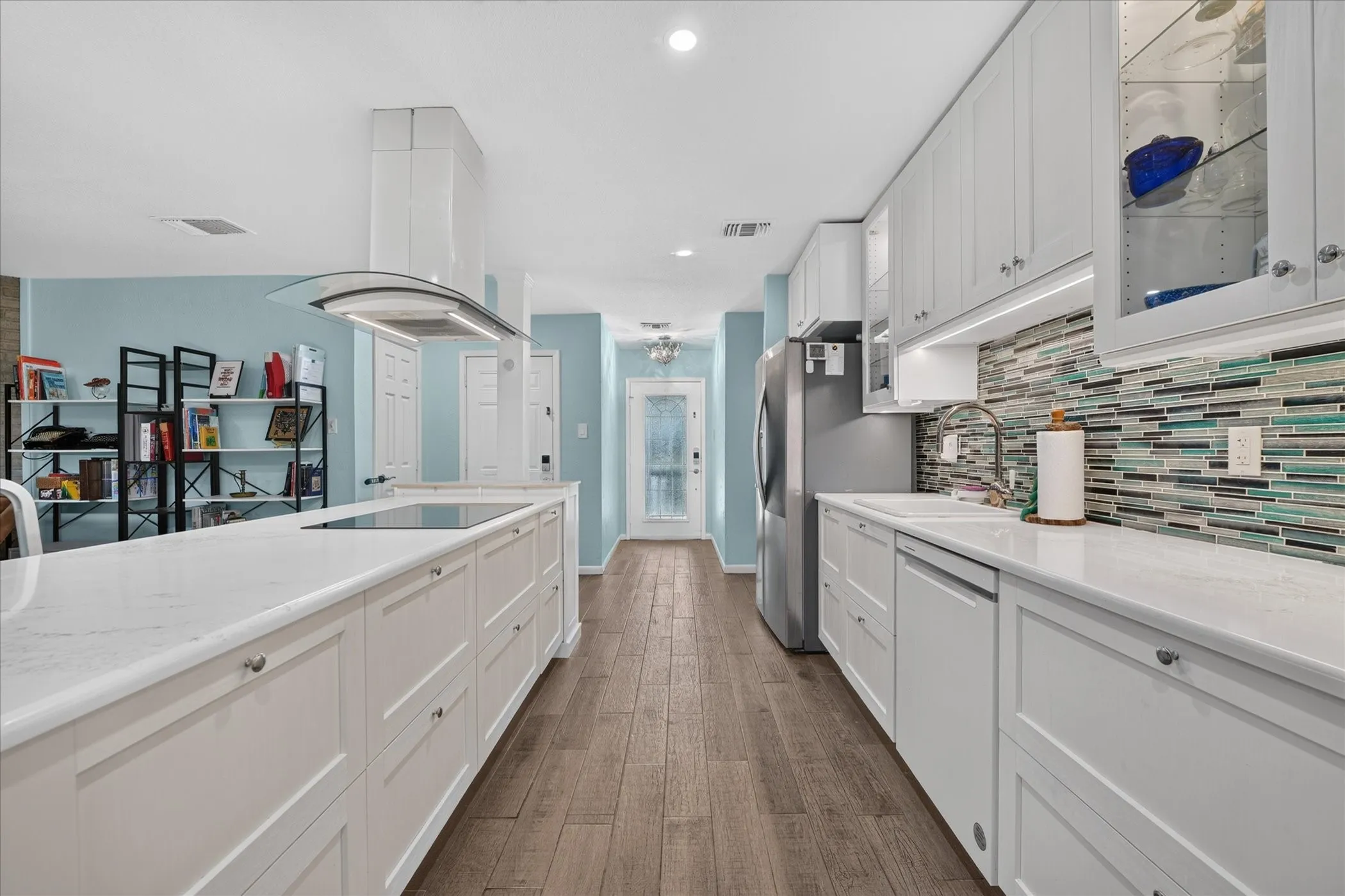 Modern kitchen featuring white cabinetry, light countertops, wood-finish flooring, a mosaic tile backsplash, and stainless steel appliances