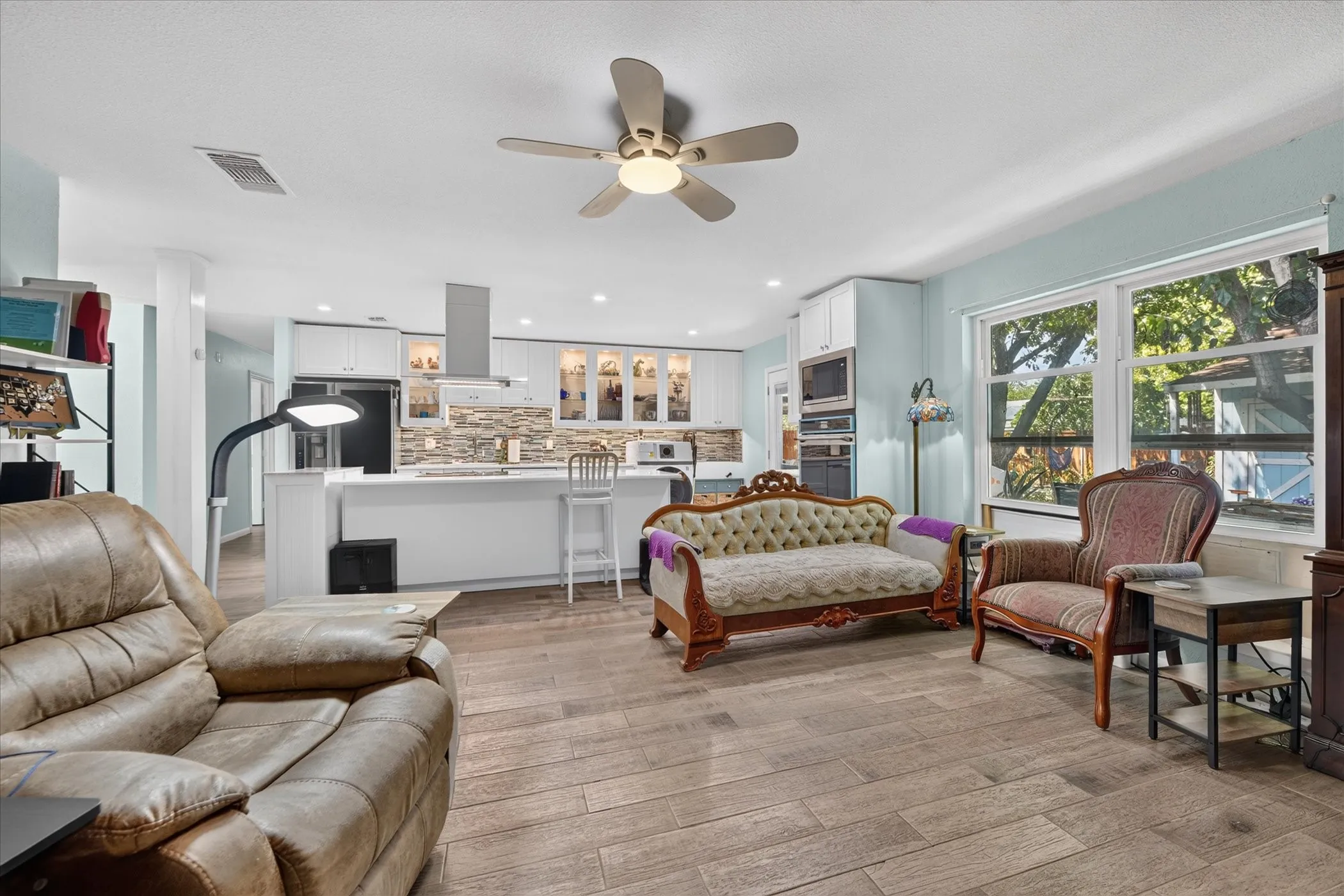 Wood-finish flooring, ceiling fan with integrated lighting, kitchen island with built-in cabinetry, stainless steel range hood, and white upper and lower cabinetry