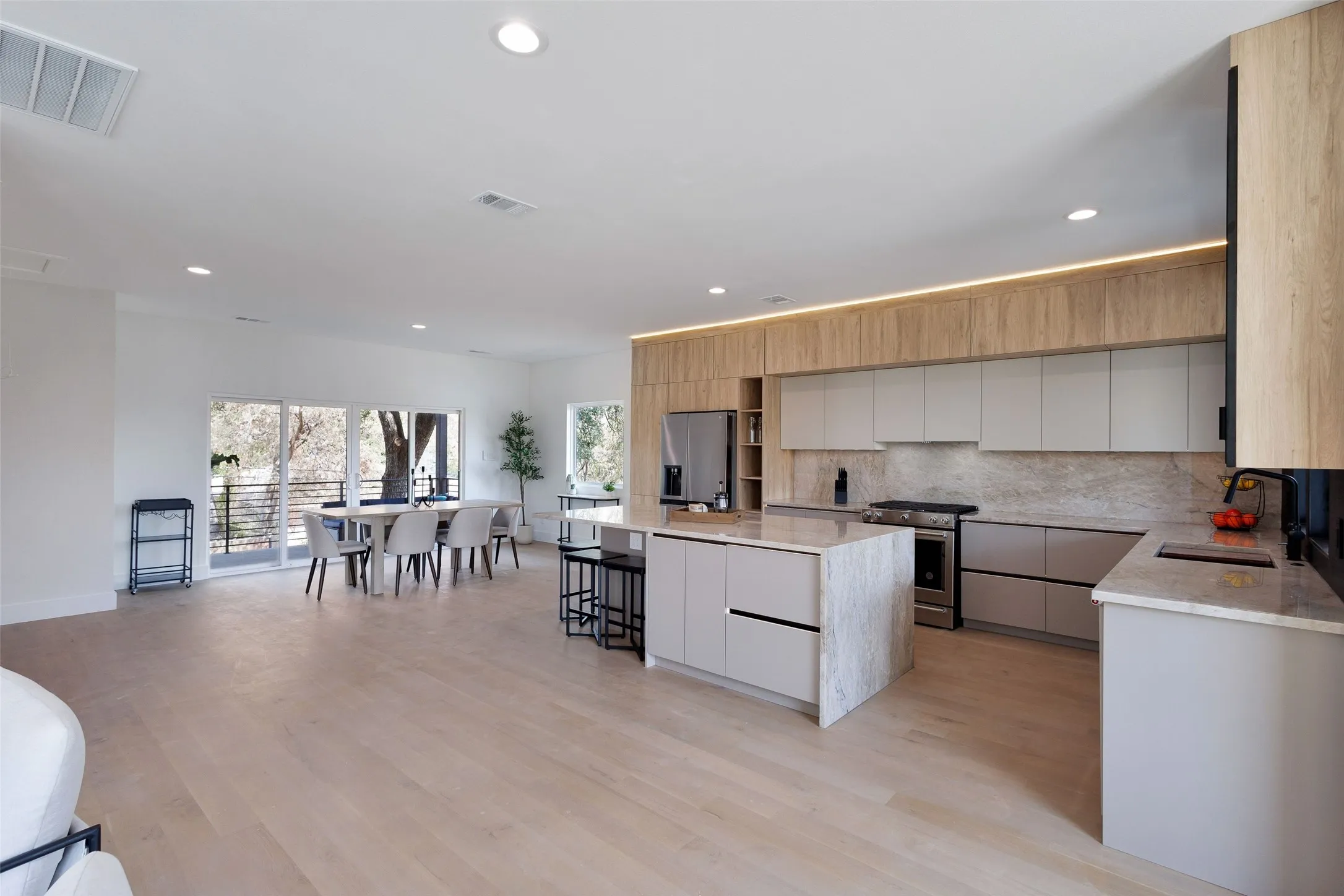 Hardwood-finish flooring throughout, recessed lighting, expansive glass sliding doors, custom cabinetry with integrated lighting, and a kitchen island with stone countertop