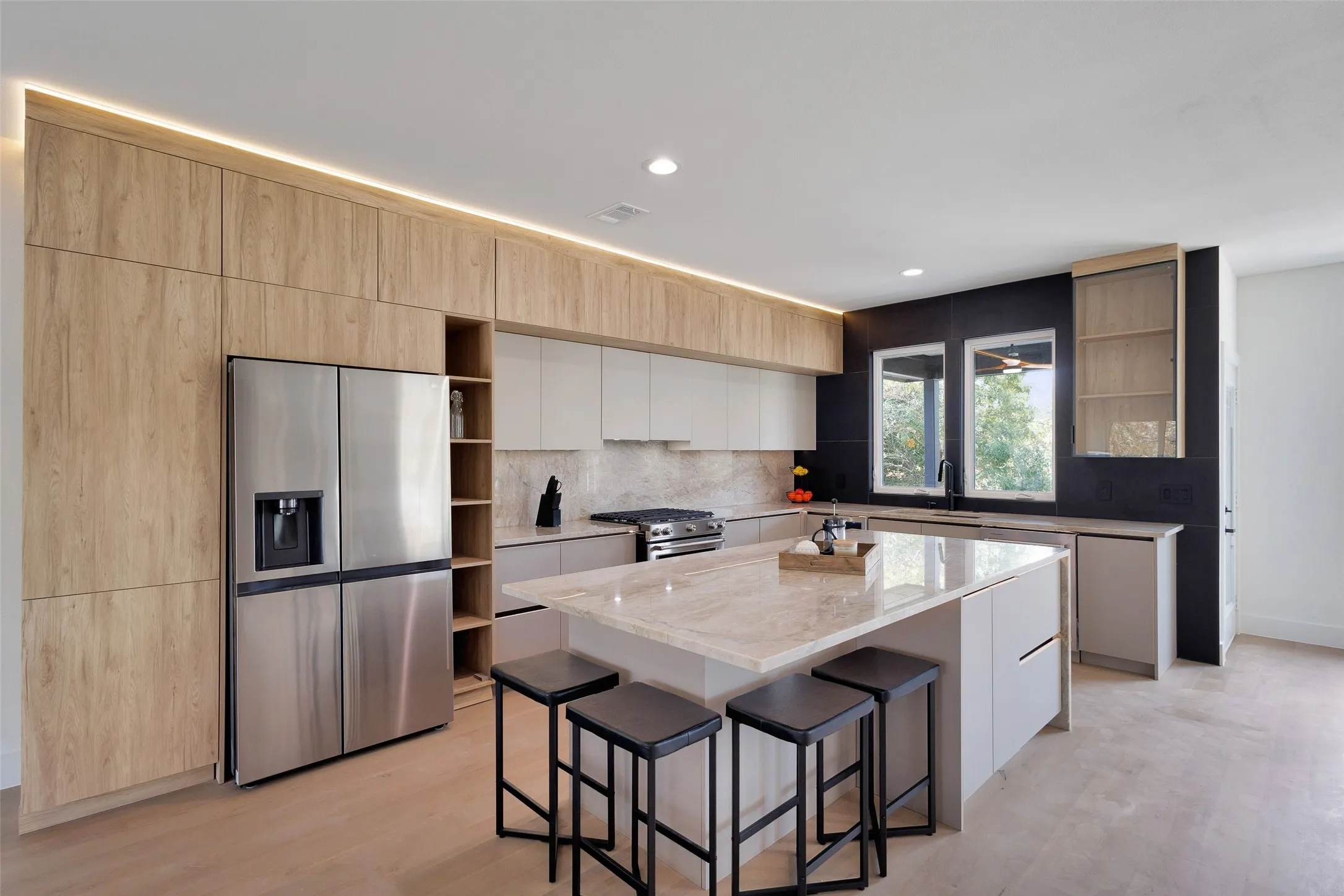 Integrated stainless steel refrigerator, light wood-finish cabinetry, central island with seating, stone countertops, and recessed lighting