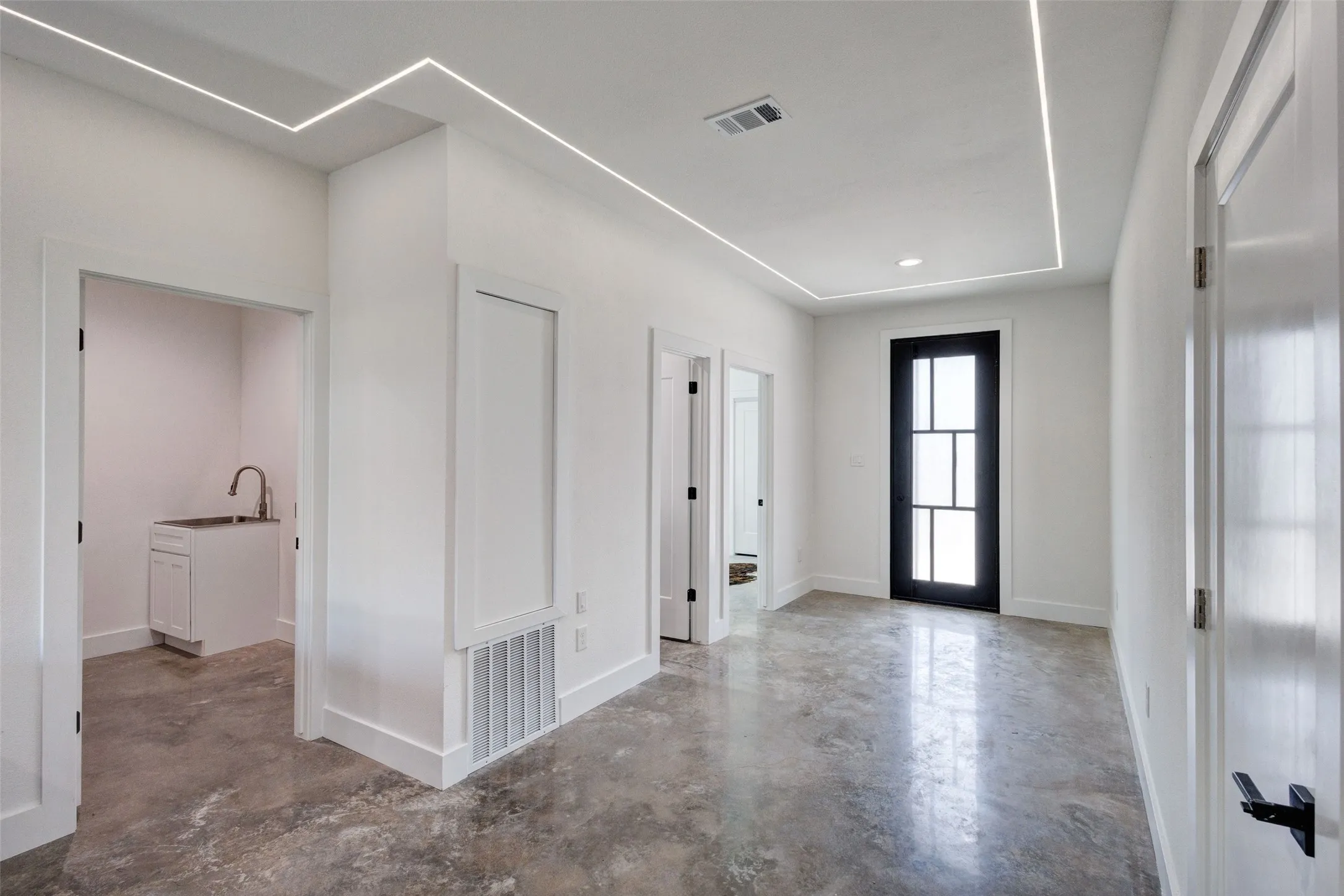 Polished concrete flooring, recessed lighting, modern black entry door with frosted glass, and white painted walls