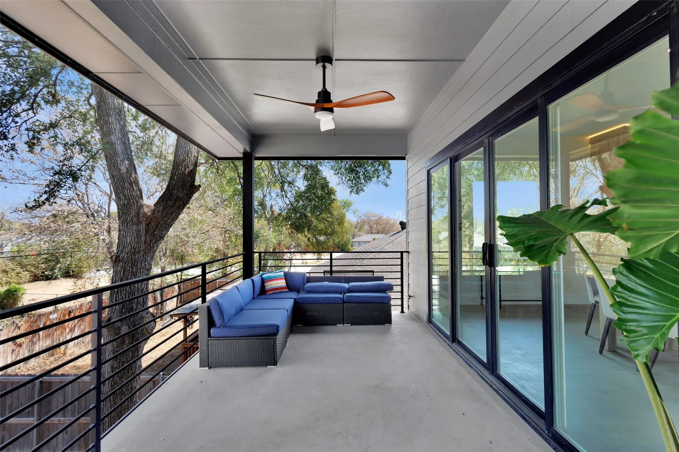 Expansive covered back balcony featuring a ceiling fan, concrete flooring, horizontal metal railings, and sliding glass doors