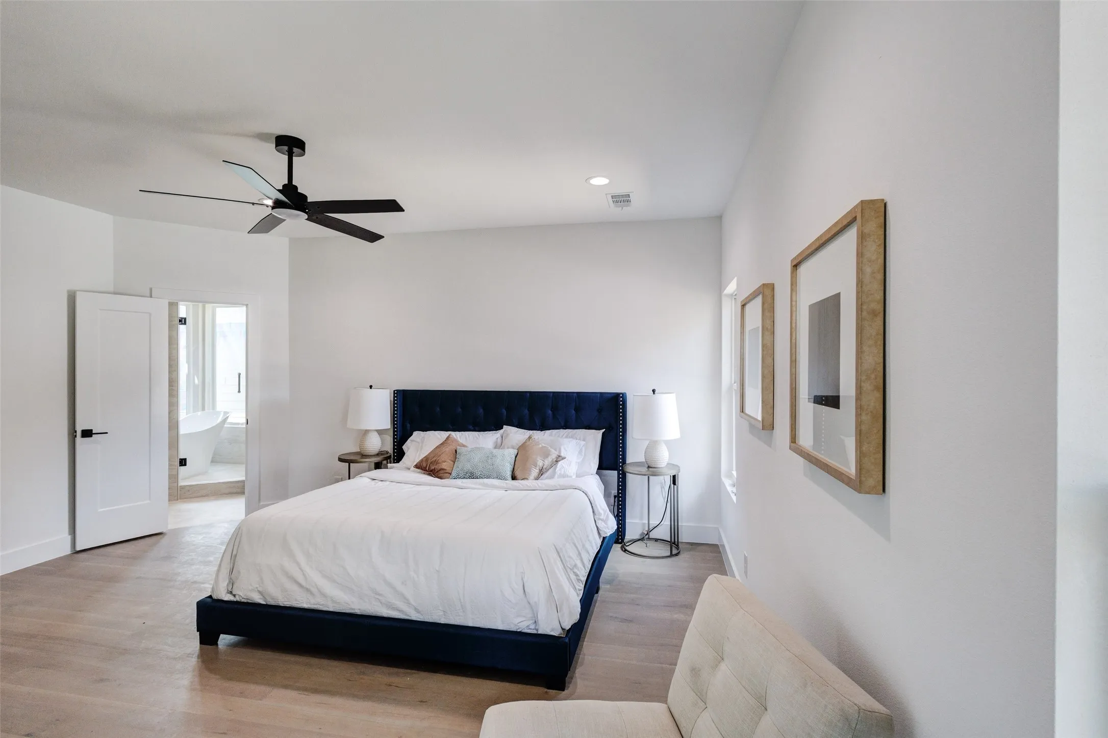 Spacious room featuring wood-finish flooring, a contemporary ceiling fan, recessed lighting, and a doorway opening to a bathroom with a freestanding tub