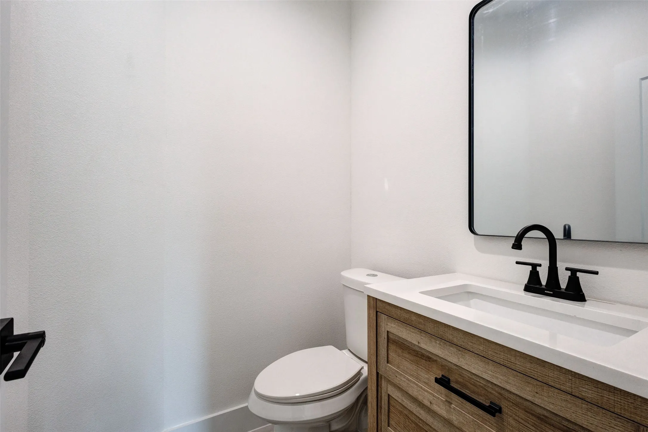 Wood-finish vanity with an integrated white sink, black faucet, and an arched black-framed mirror