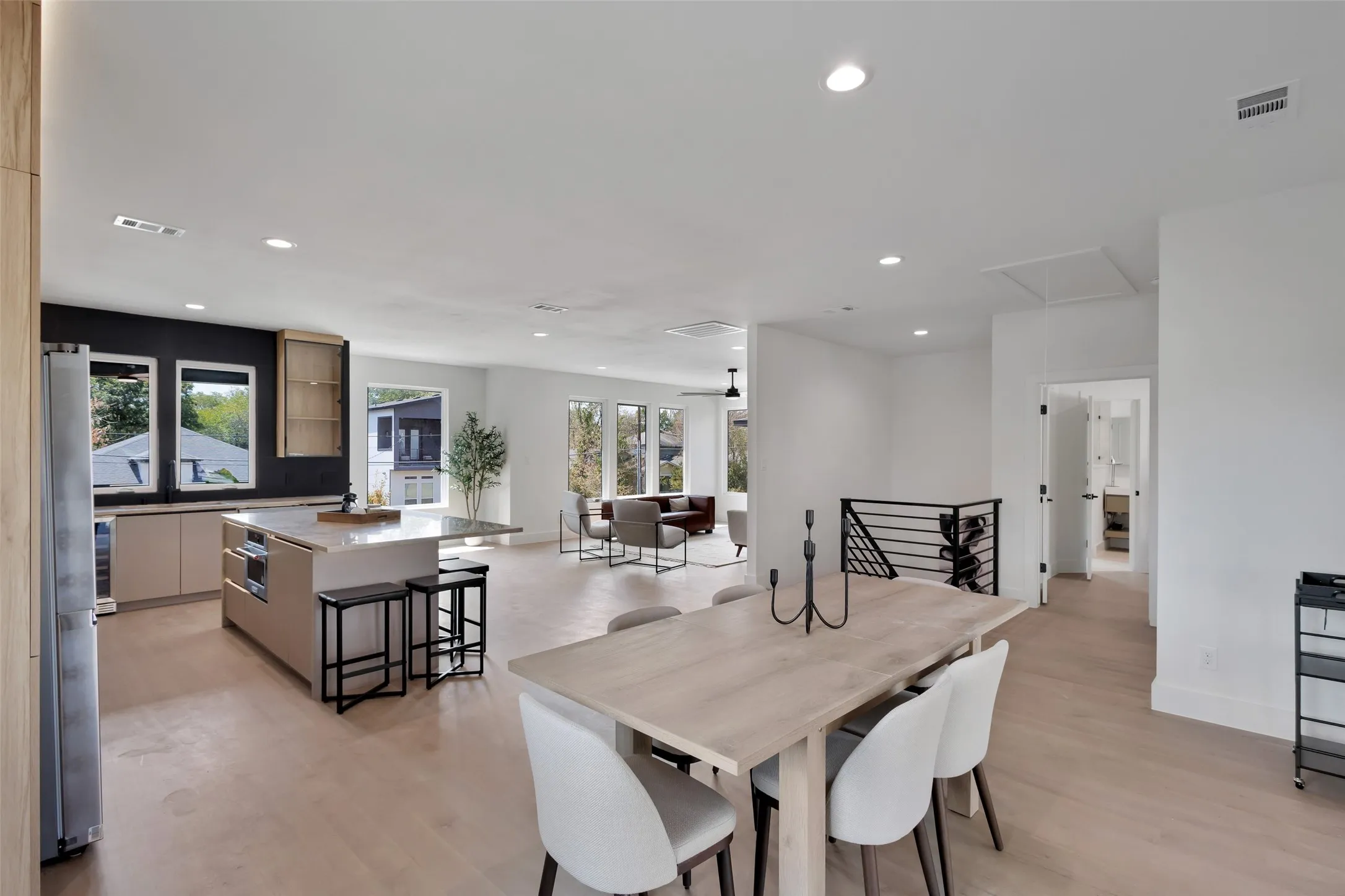 Open concept living area featuring a kitchen island with seating, recessed lighting, wood-finish flooring, and a contemporary metal railing