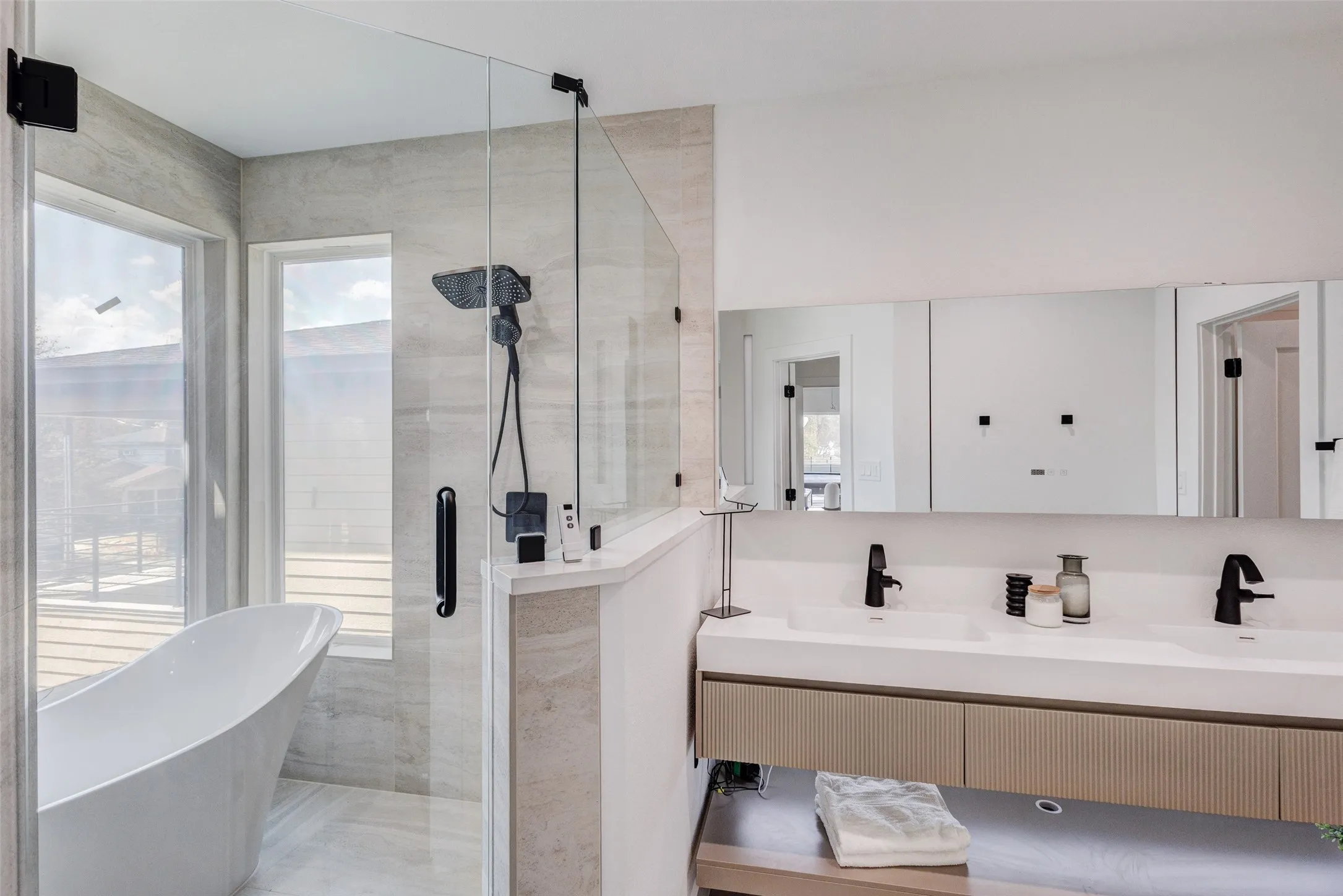 Glass-enclosed shower with a rainfall showerhead, freestanding soaking tub, dual vanity with undermount sinks, and wall-mounted mirrors