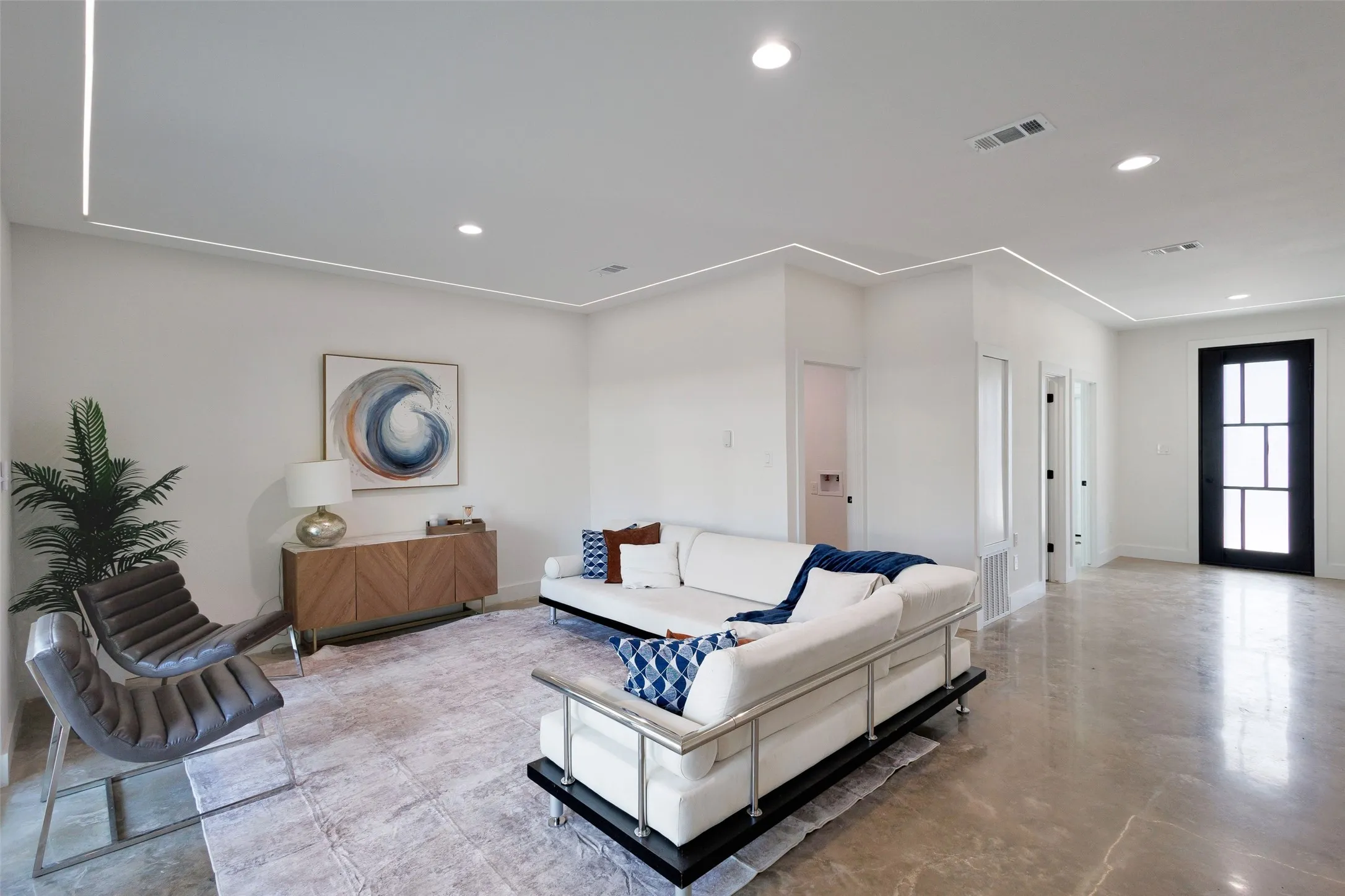 Recessed ceiling lighting, linear accent lighting, bright white walls, dark-framed entry door with glass panels, and polished concrete flooring