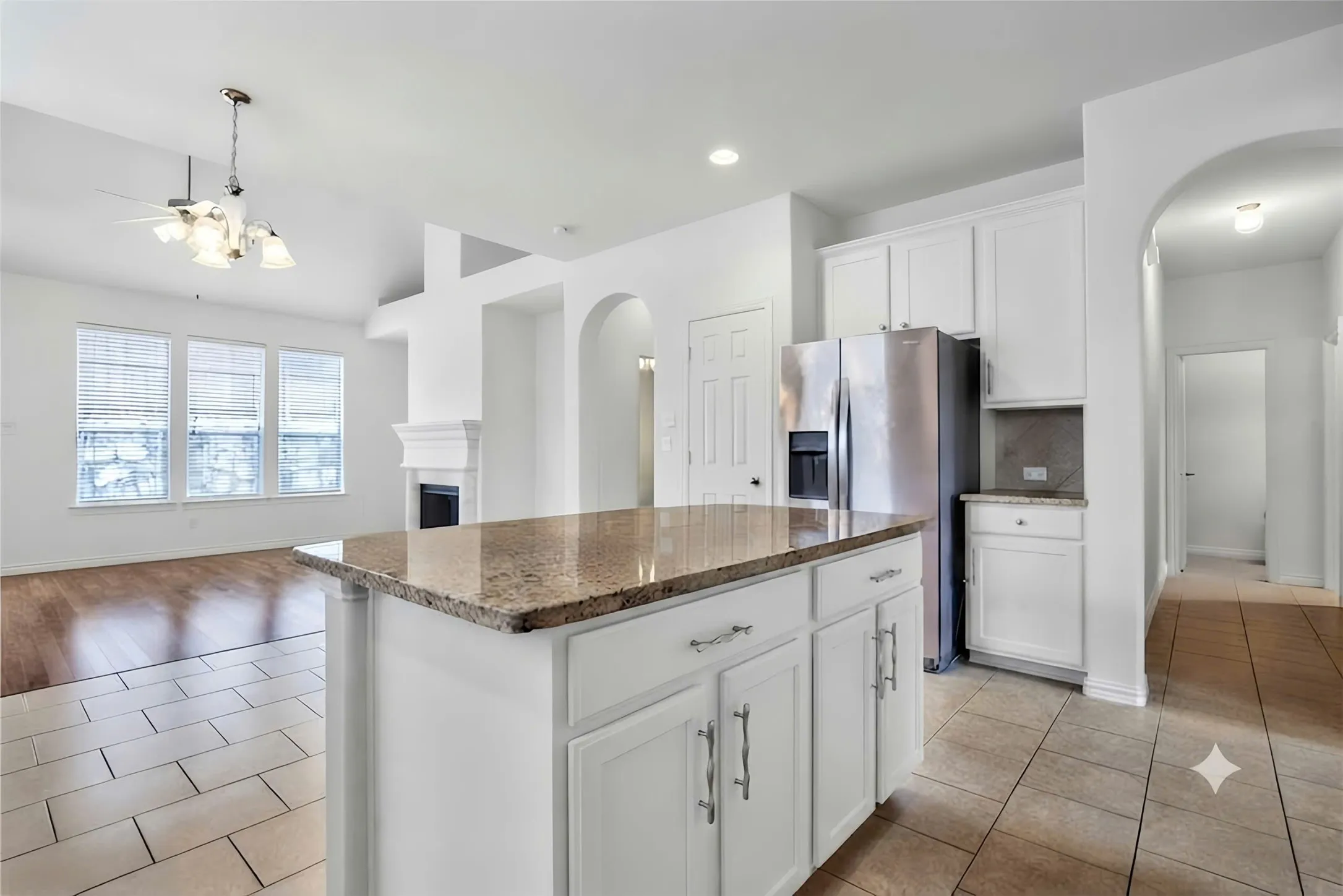 Kitchen island with granite countertop and white cabinetry, integrated stainless steel refrigerator, arched doorways, fireplace with mantel, and wood-finish flooring