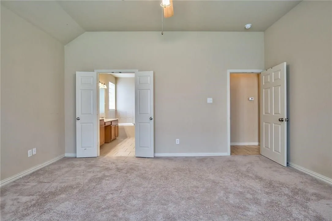Vaulted ceiling with a ceiling fan, carpeted flooring, and neutral wall tones