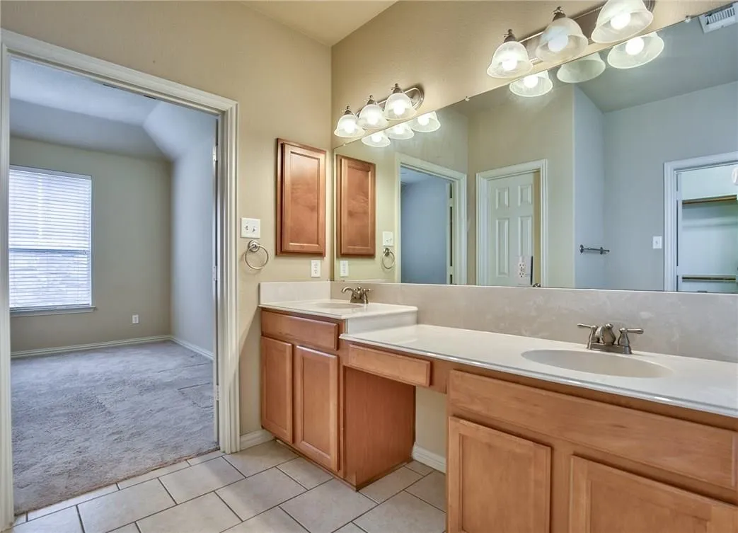 Double vanity with integrated sinks, ample countertop space, wood-finish cabinetry, and ceramic tile flooring
