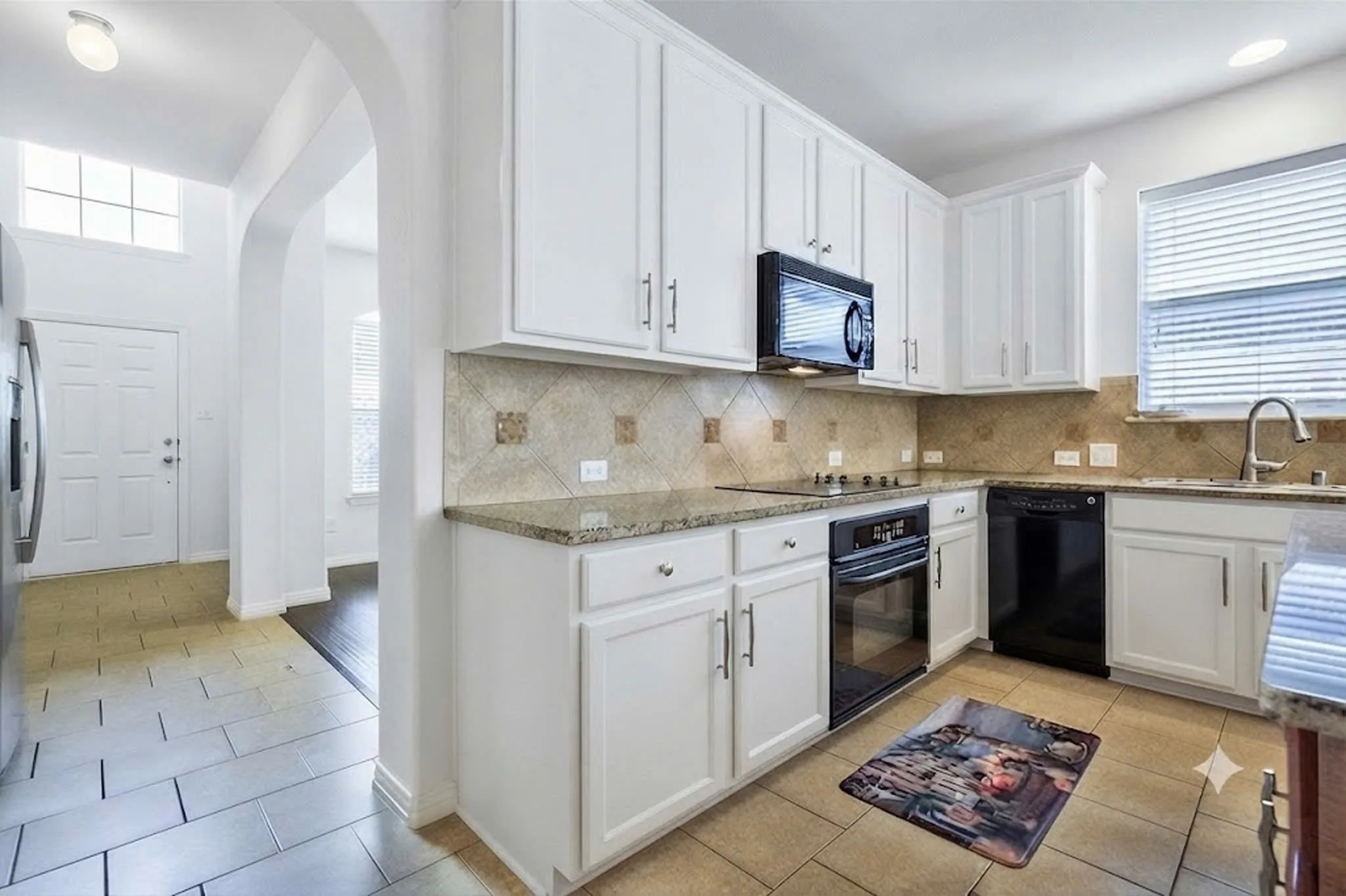 Kitchen featuring white cabinetry, granite countertops, tile backsplash, stainless steel sink with gooseneck faucet, and integrated black appliances
