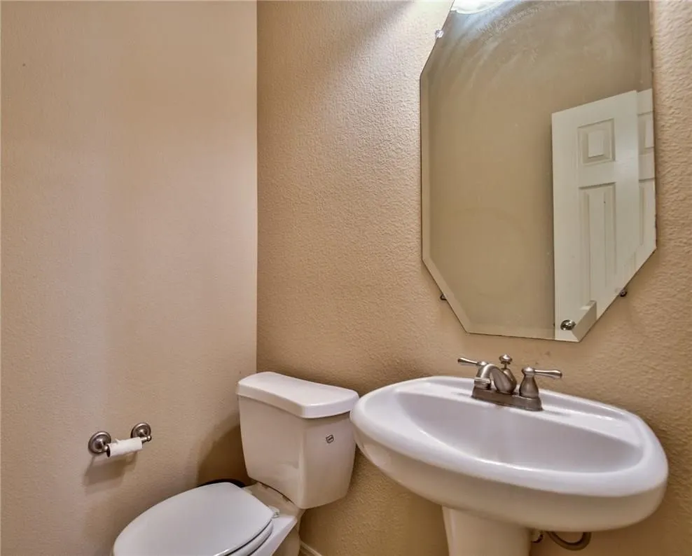 Pedestal sink, wall-mounted mirror with beveled edges, and a two-piece toilet