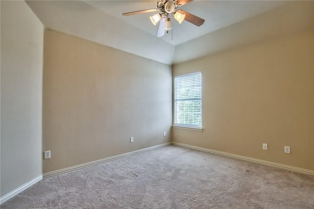 Vaulted ceiling with a ceiling fan light fixture, neutral carpeting, and a window with blinds