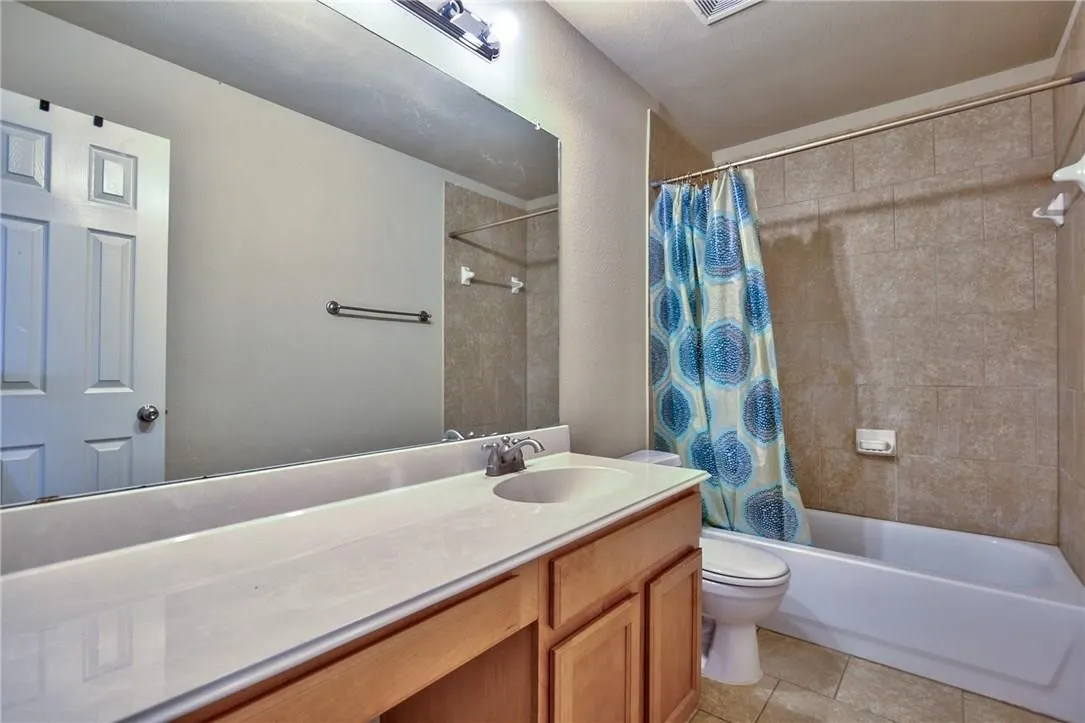 Bathroom featuring a white vanity with integrated sink, light wood-finish cabinetry, a large wall mirror, and a tiled shower/tub combination