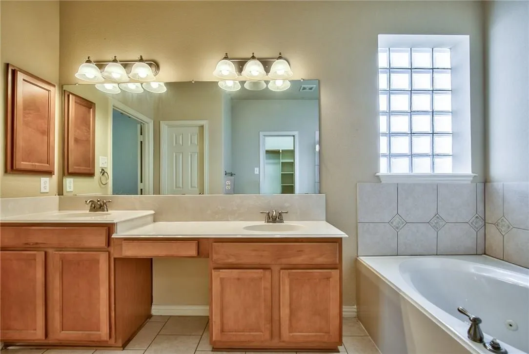 Dual wood-finish vanities with integrated sinks, a large wall-mounted mirror, and a built-in jetted tub