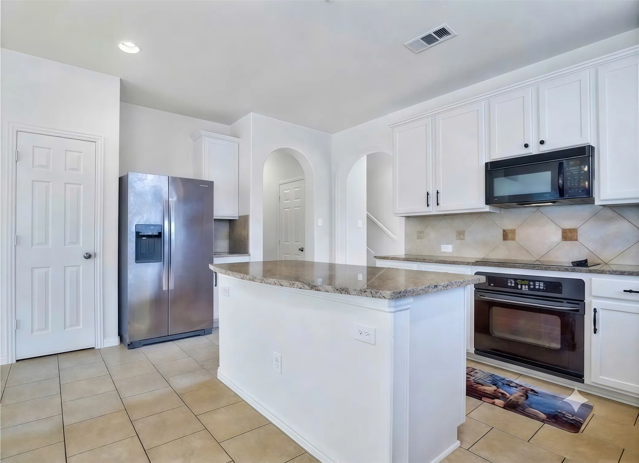 Kitchen featuring white cabinetry, a central island with a stone countertop, tile flooring, and a tile backsplash