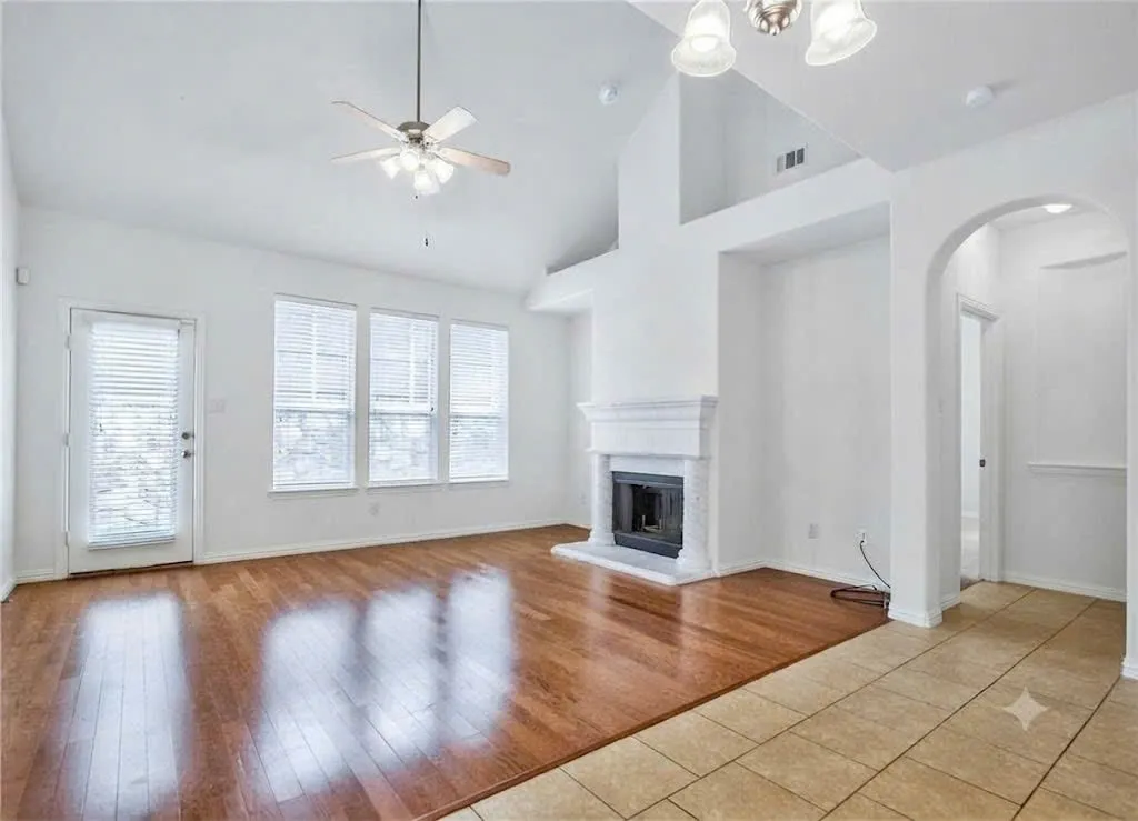Vaulted ceilings, wood-finish flooring, fireplace with white mantel, multiple windows, and a ceiling fan