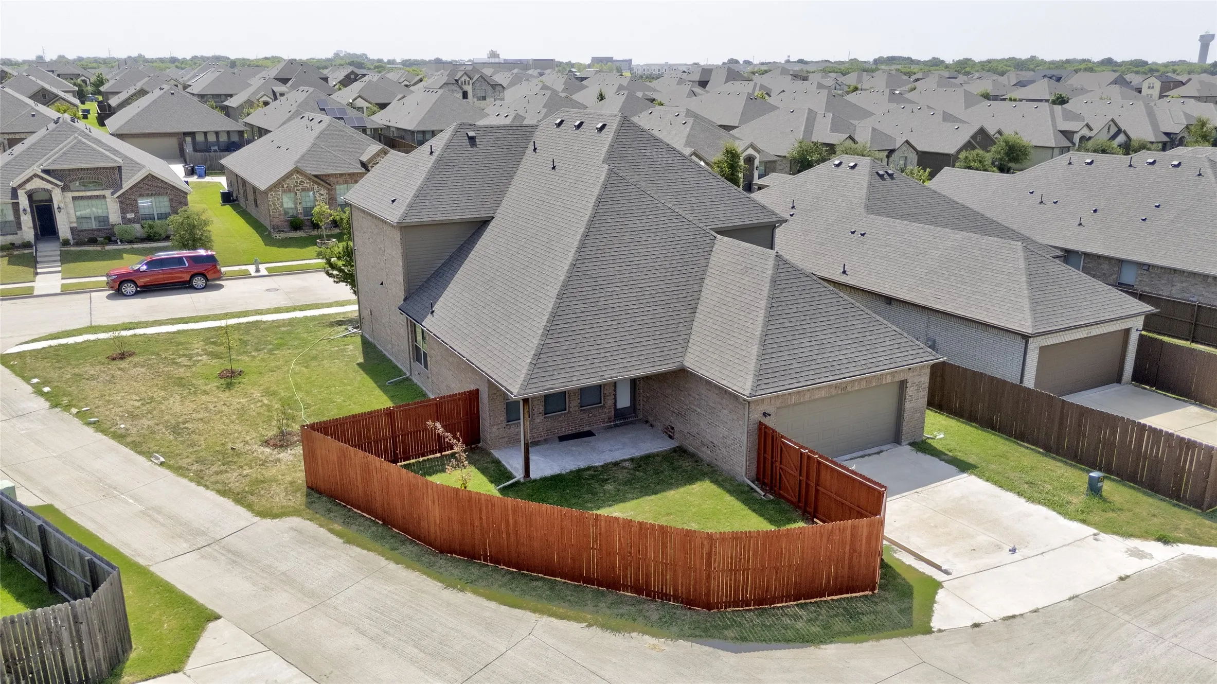 Aerial view of the covered back patio, fenced backyard, and rear-entry two-car garage