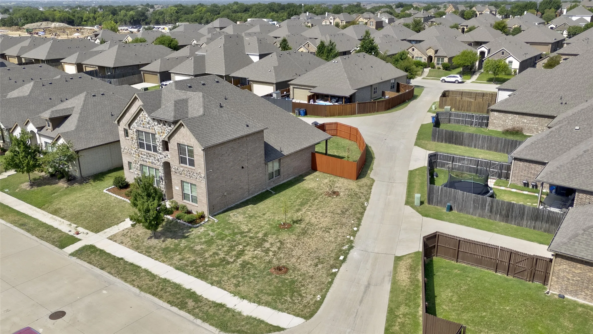 Aerial view of the corner lot with side yard, stained wood fence, and brick and stone exterior