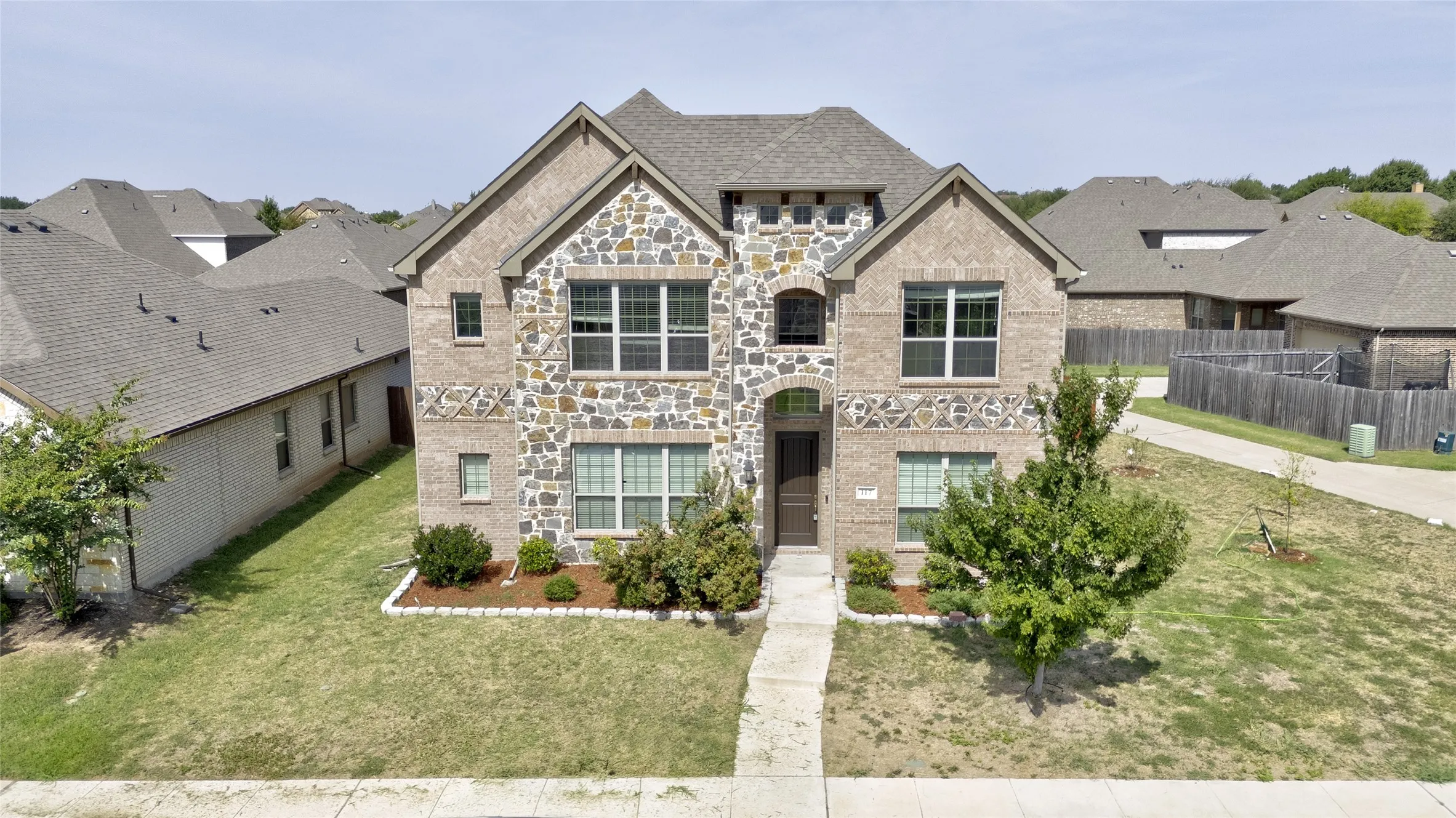 Front of this Red Oak TX home with stone and brick facade, arched front door, and landscaped beds