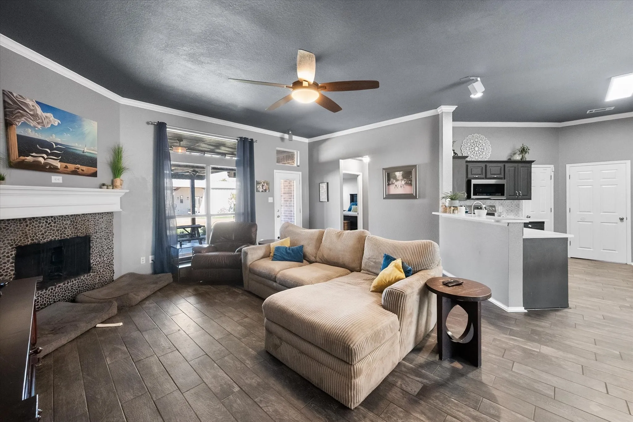 Wood-finish flooring throughout, fireplace with stone surround and white mantel, ceiling fan, and track lighting
