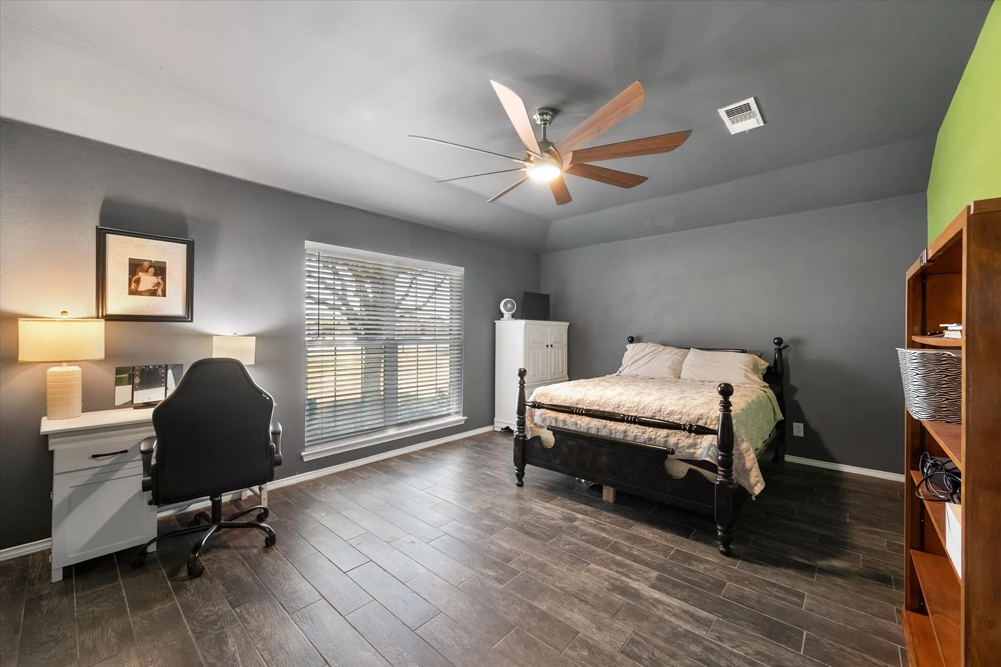 Wood-finish flooring, vaulted ceiling, ceiling fan with light, large window with blinds, and built-in shelving