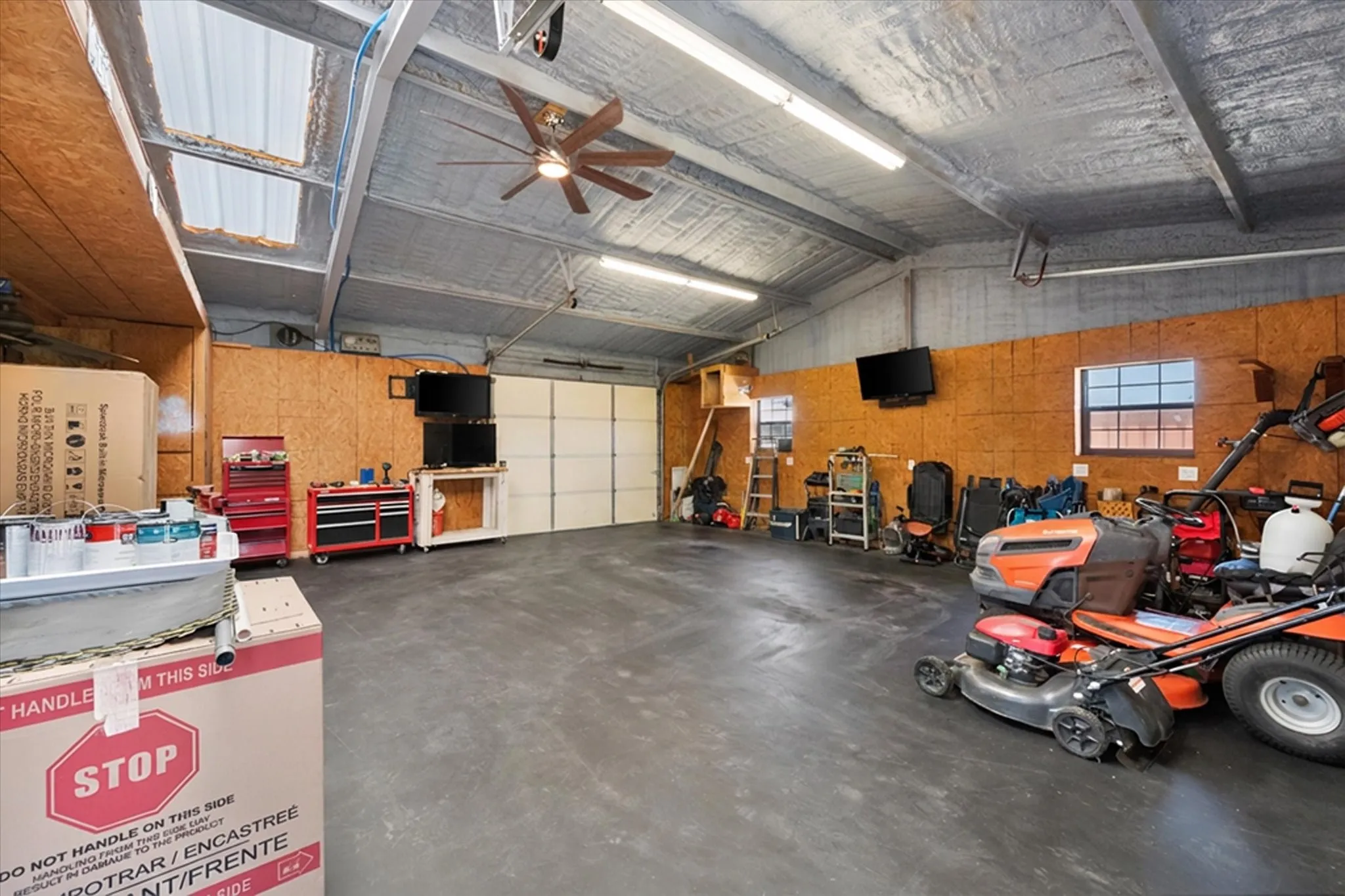 Spacious garage featuring a ceiling fan, dual skylights, multiple windows, ample task lighting, and a large garage door